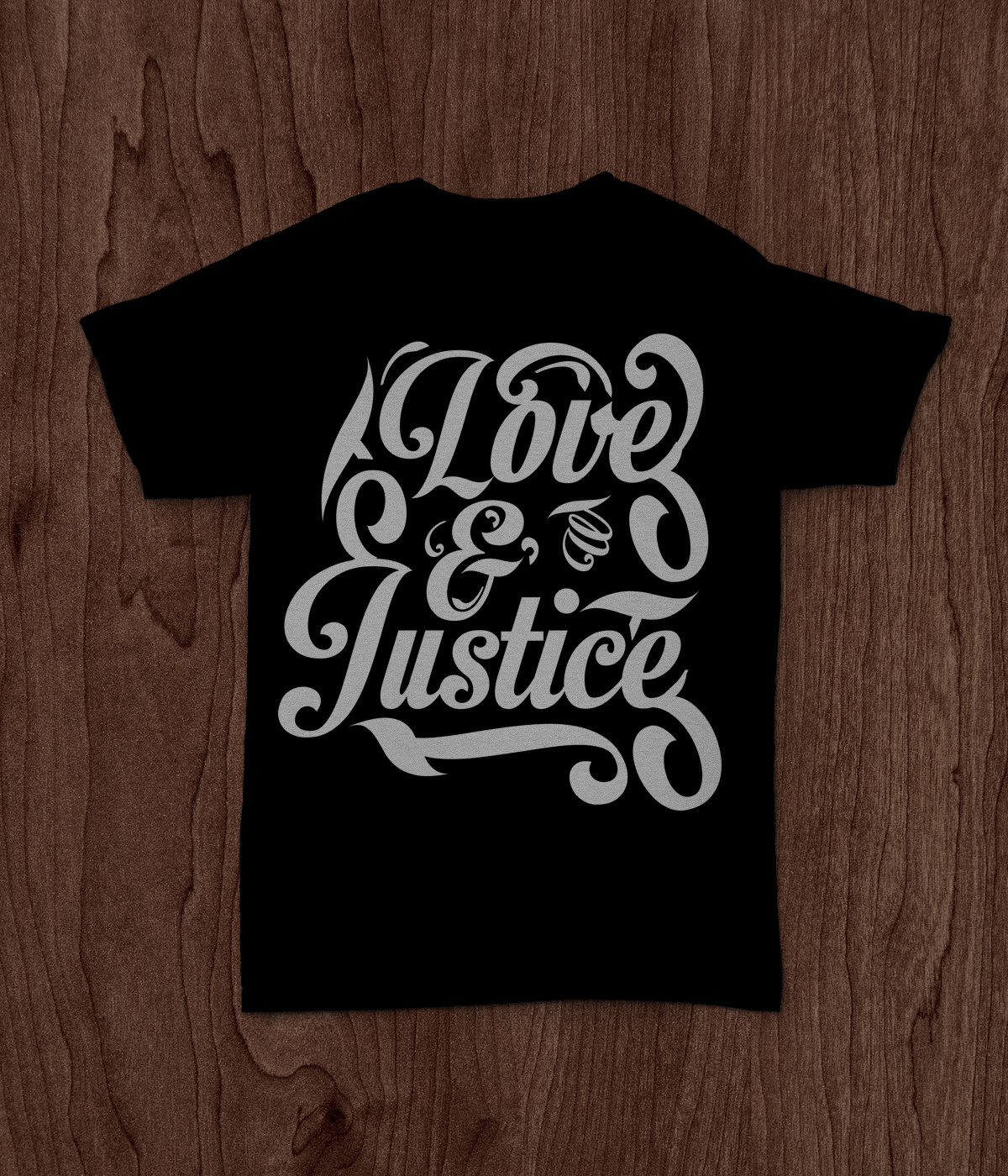 Photo of a black t-shirt laying on top of a wood table. The text reads Love and Justice in a stylized font.