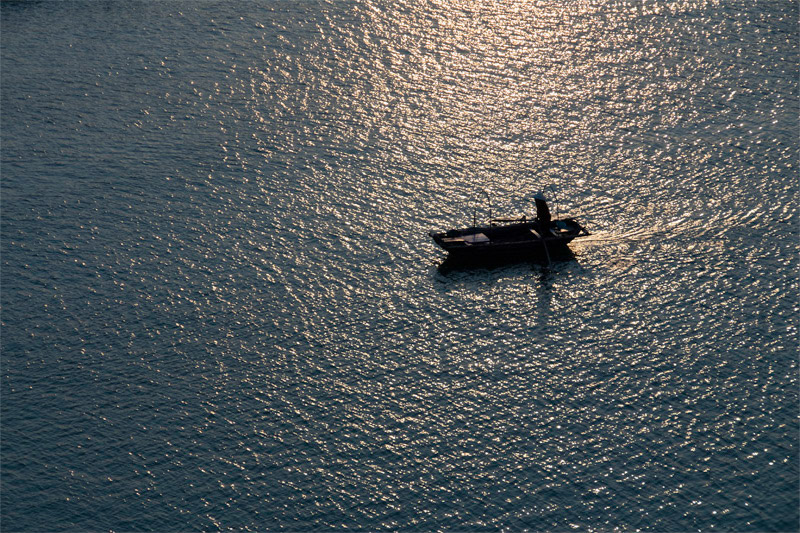 Oarsman rowing in the twilight at Cat Ba Harbor