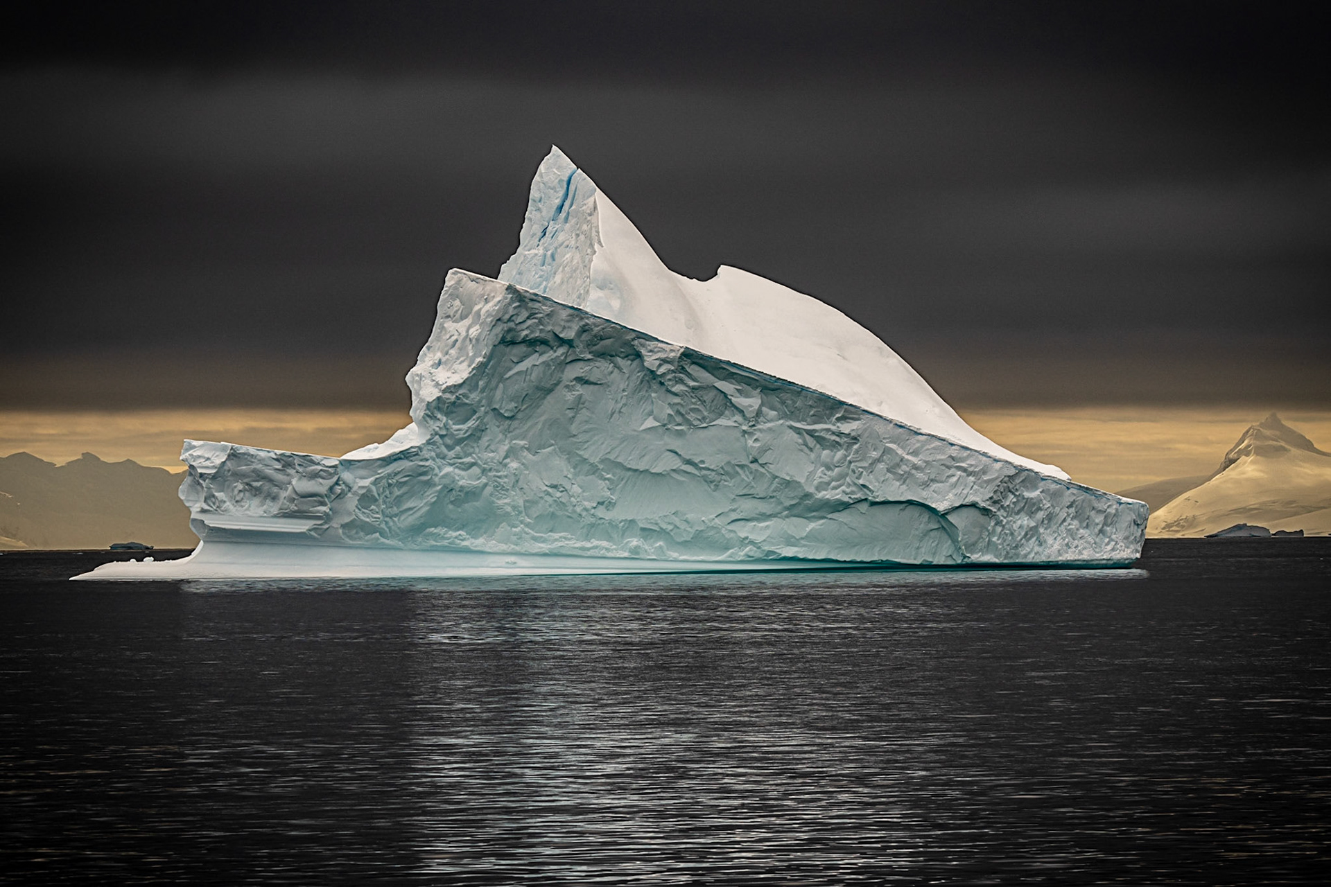 Ragged iceberg shining in sun with black sky and sea
