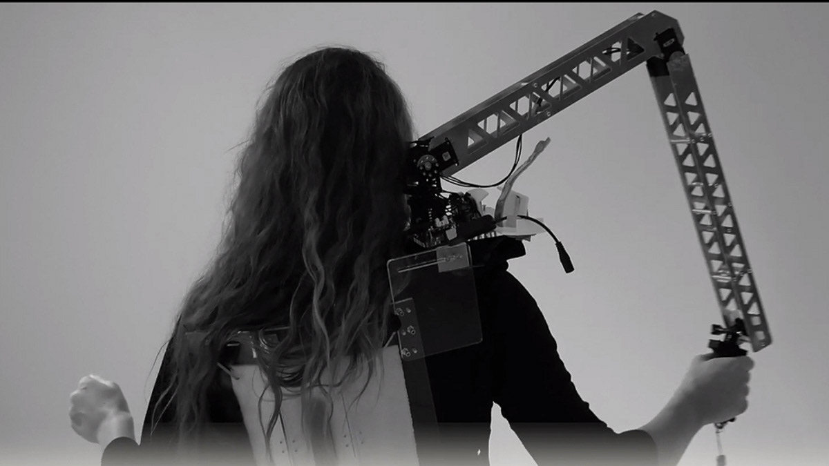The robotic arm is attached to a wearable black plate, which is also used to mount a battery pack and other necessary electronics. The arm sits comfortably on the shoulder and can extend a full arms length