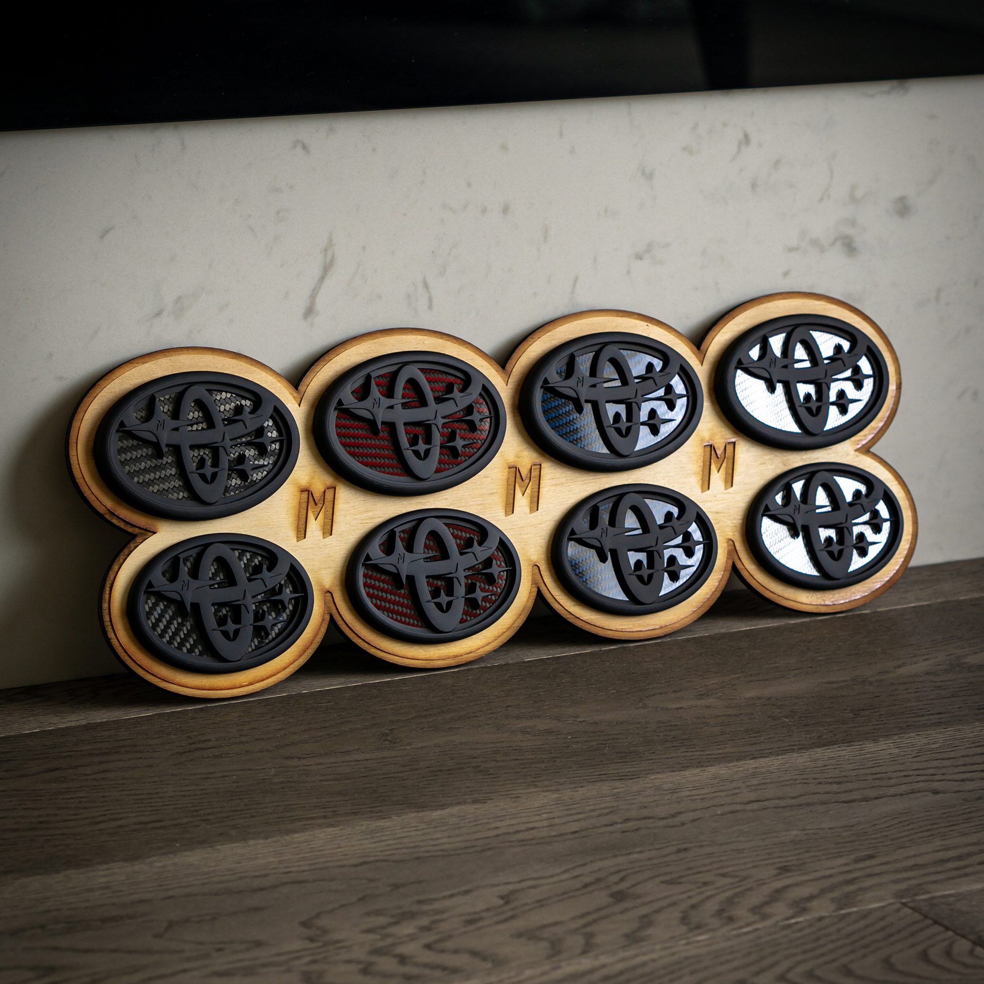 Collection of Toyota-Subaru combination emblems with black, red, blue, and silver carbon fiber backing.
