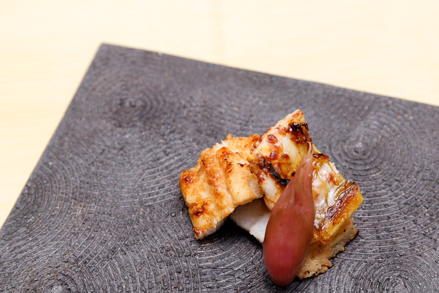 黒い器に盛り付けた焼き魚とミョウガの料理写真。食材の焼き色と質感を表現したフードフォト。