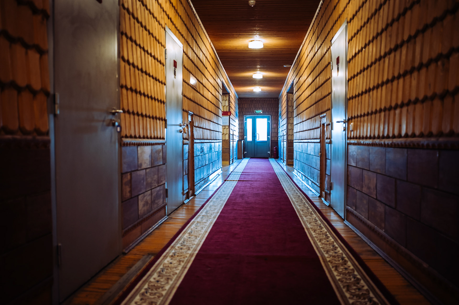 Ein langer Hotelkorridor mit hölzernen Wänden und einem roten Teppich in Pyramiden. Die Beleuchtung verstärkt die warme und rustikale Atmosphäre.