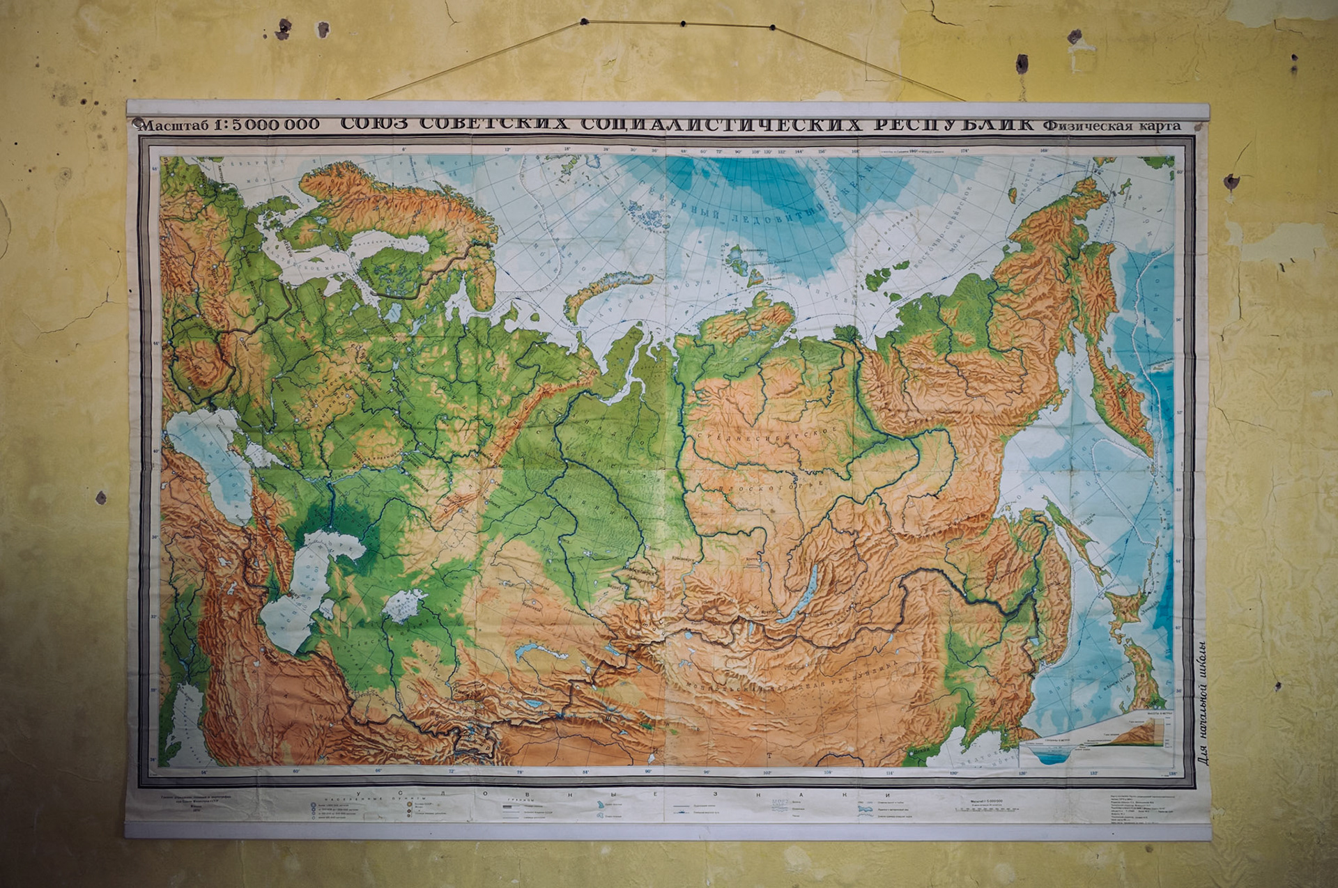 Eine alte physische Karte der Sowjetunion hängt an einer gelben Wand in der verlassenen Schule von Pyramiden. Sie zeigt topographische Details der UdSSR und verweist auf den historischen Kontext der Stadt.