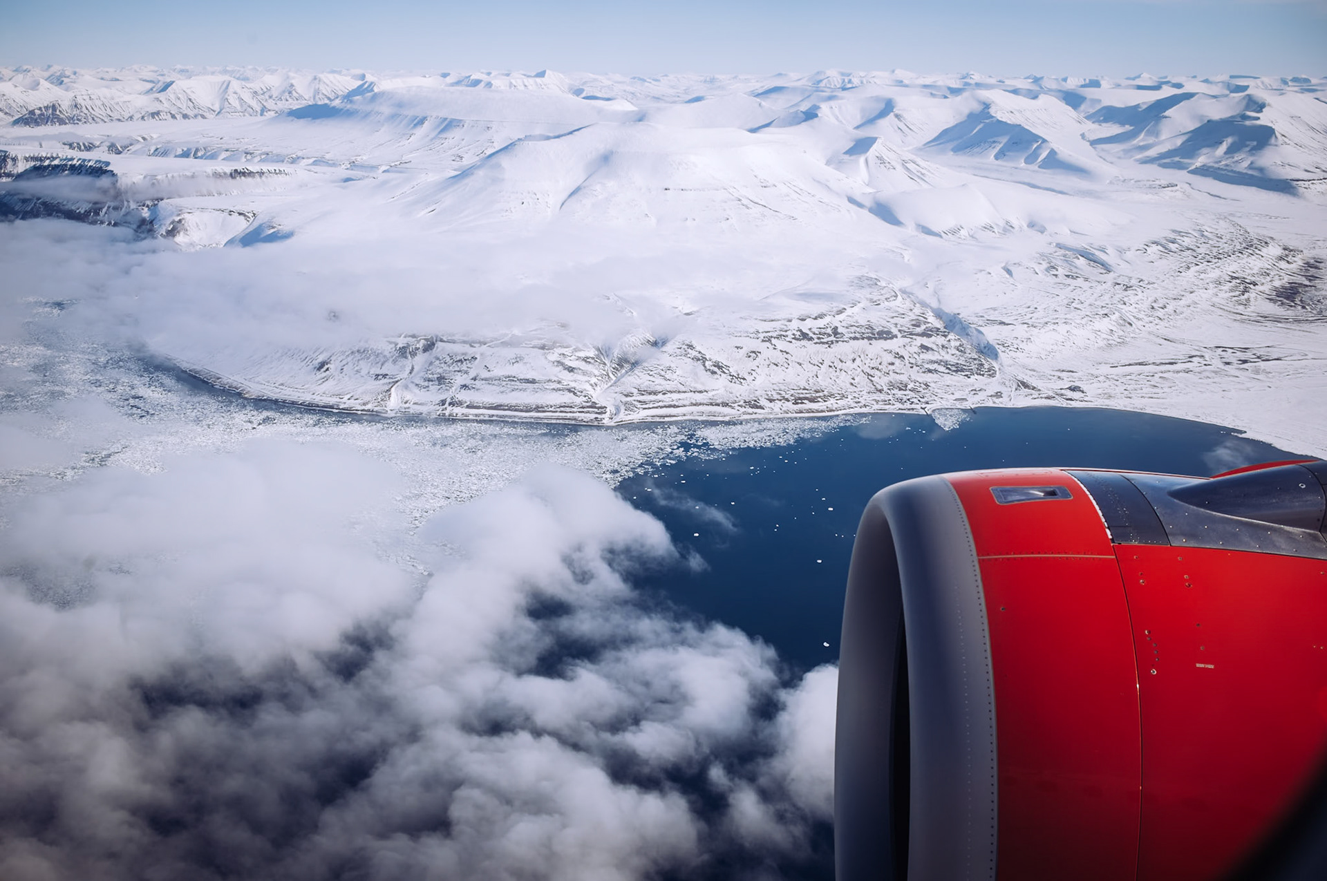 Diese Luftaufnahme zeigt die verschneiten Berge rund um Longyearbyen, mit einem Flugzeugflügel im Vordergrund. Die Szenerie vermittelt ein Gefühl von Abgeschiedenheit und der extremen arktischen Landschaft.
