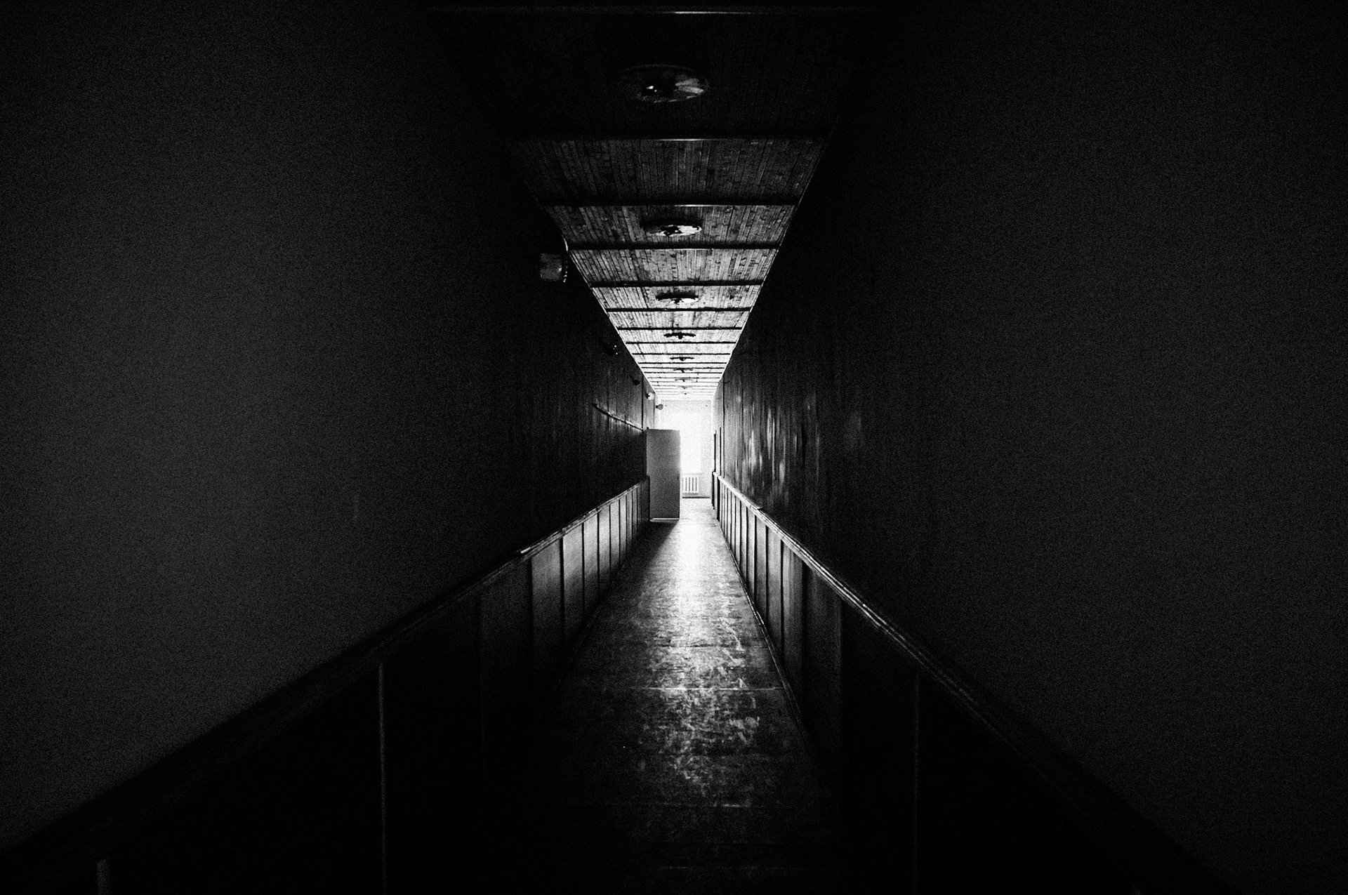 Ein langer dunkler Flur in der verlassenen Schule von Pyramiden führt zu einem hell erleuchteten Ausgang. Die beklemmende Atmosphäre verstärkt den Eindruck der Vergänglichkeit dieser einstigen Bildungsstätte.
