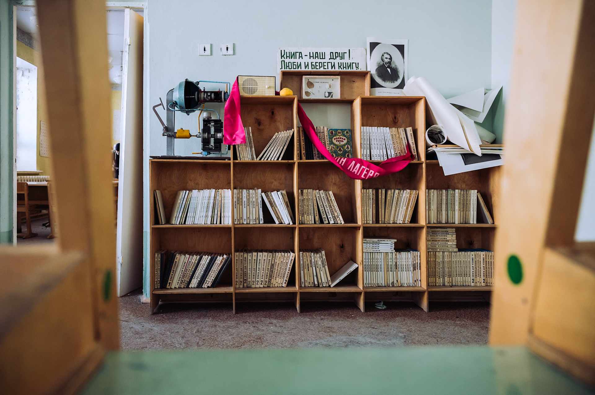 Ein verlassenes Bücherregal mit sowjetischen Lehrbüchern steht in einem ehemaligen Klassenzimmer in Pyramiden. Über den Büchern hängt ein rotes sozialistisches Banner mit russischer Aufschrift.