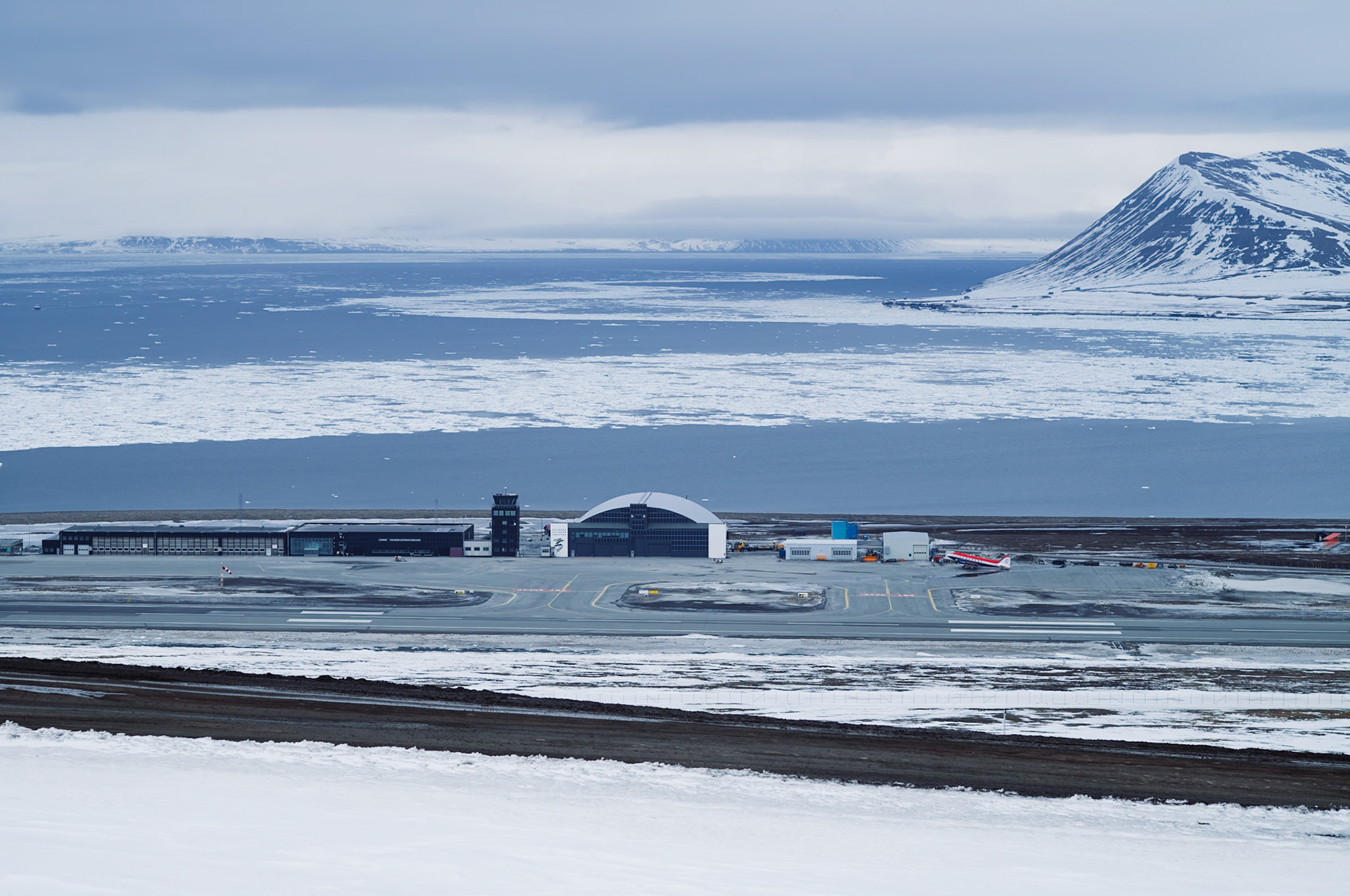 Der Flughafen von Longyearbyen ist von schneebedeckten Bergen und dem Meer umgeben. Einige Flugzeuge stehen auf dem Rollfeld.