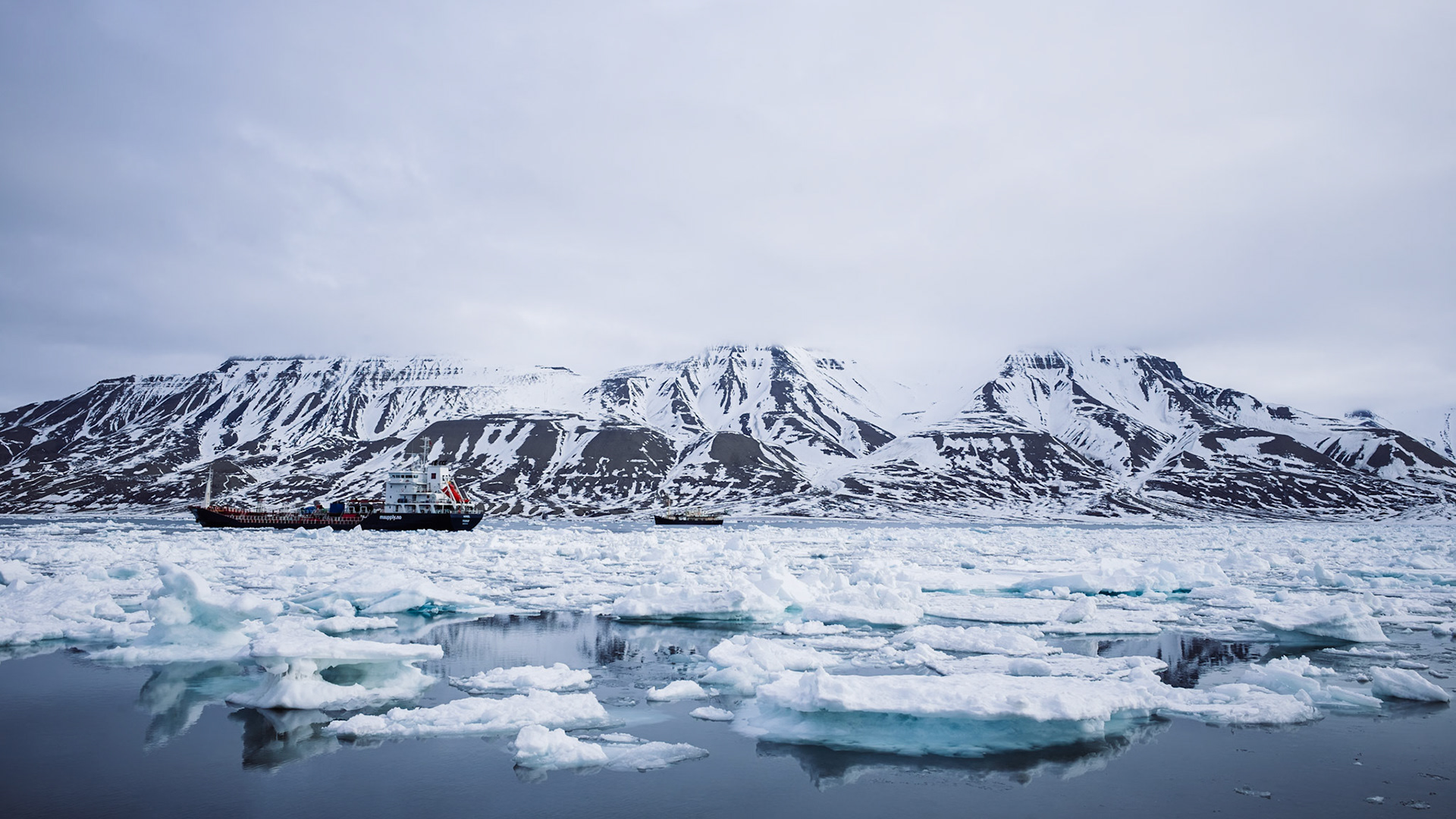 Ein Frachtschiff liegt im arktischen Eis vor schneebedeckten Bergen. Die Szenerie zeigt die majestätische Schönheit des hohen Nordens.