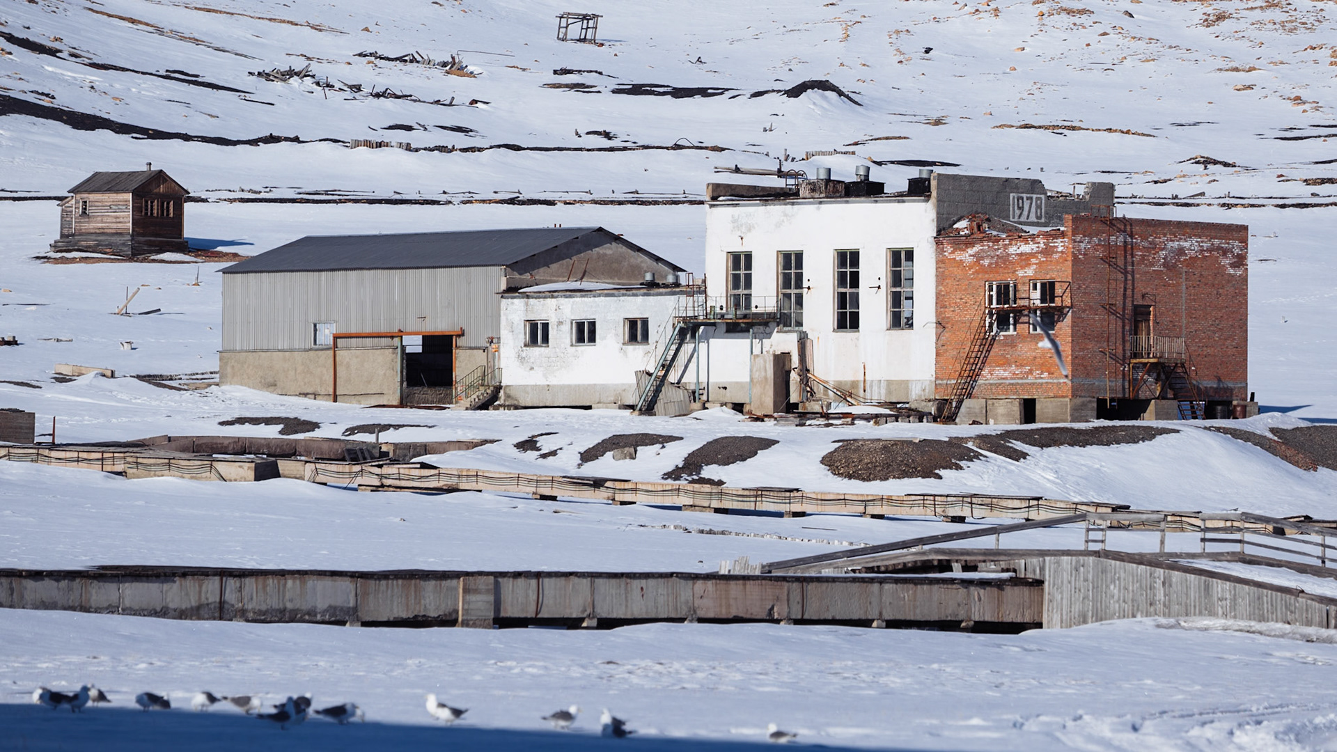 Verlassene Industrieanlagen mit Gebäuden und einem verwitterten Rohrsystem in der Nähe von Pyramiden.