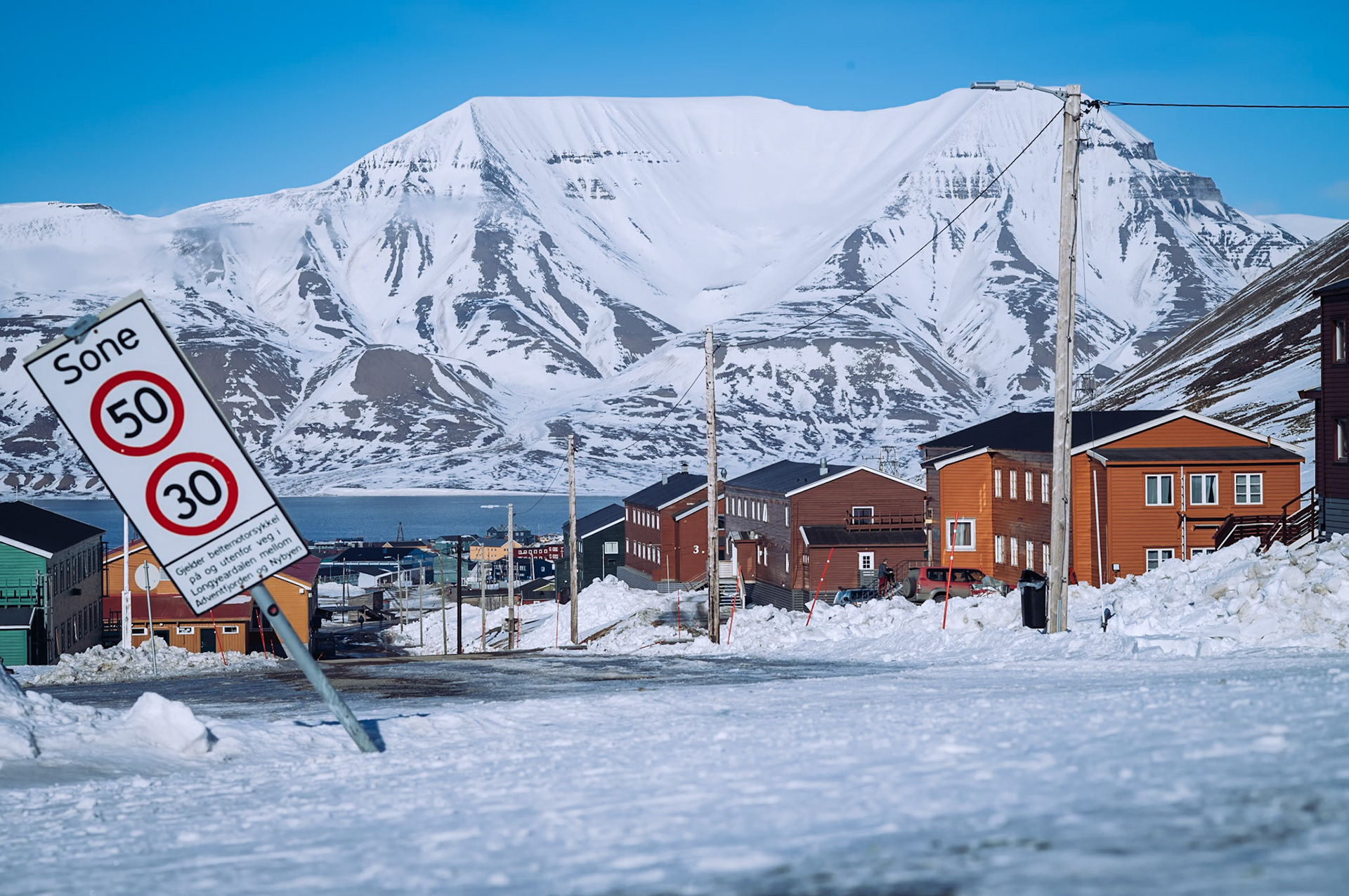 Eine kleine Ansammlung von bunten Holzhäusern in Longyearbyen mit einer majestätischen Bergkette im Hintergrund. Die verschneite Landschaft und klare Luft vermitteln die typische Atmosphäre Spitzbergens.