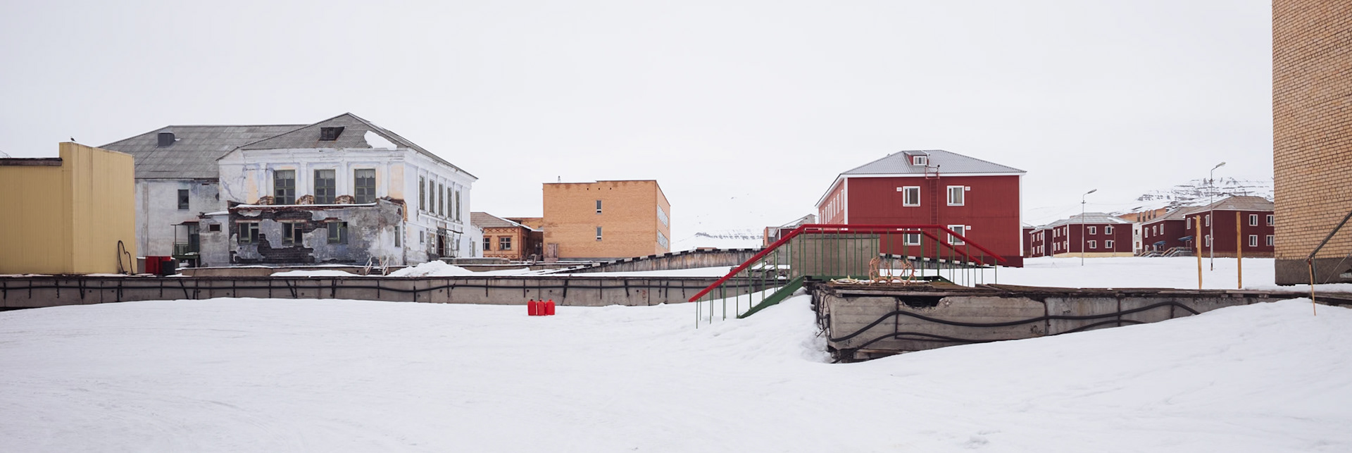 Mehrere Gebäude in Pyramiden, teils verlassen, teils renoviert, umgeben von schneebedecktem Gelände. Eine Mischung aus verfallenen und neueren Strukturen prägt das Bild.