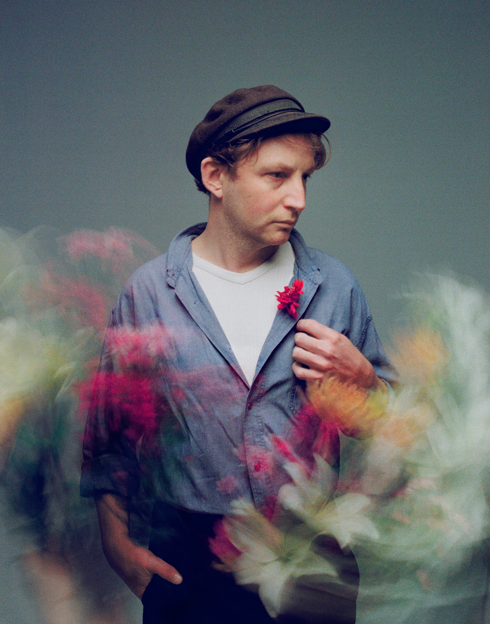 John wears a vintage woollen Breton hat, blue-grey shirt and a flower in his lapel. Images 'float' in a long exposure of motion blurred around him.