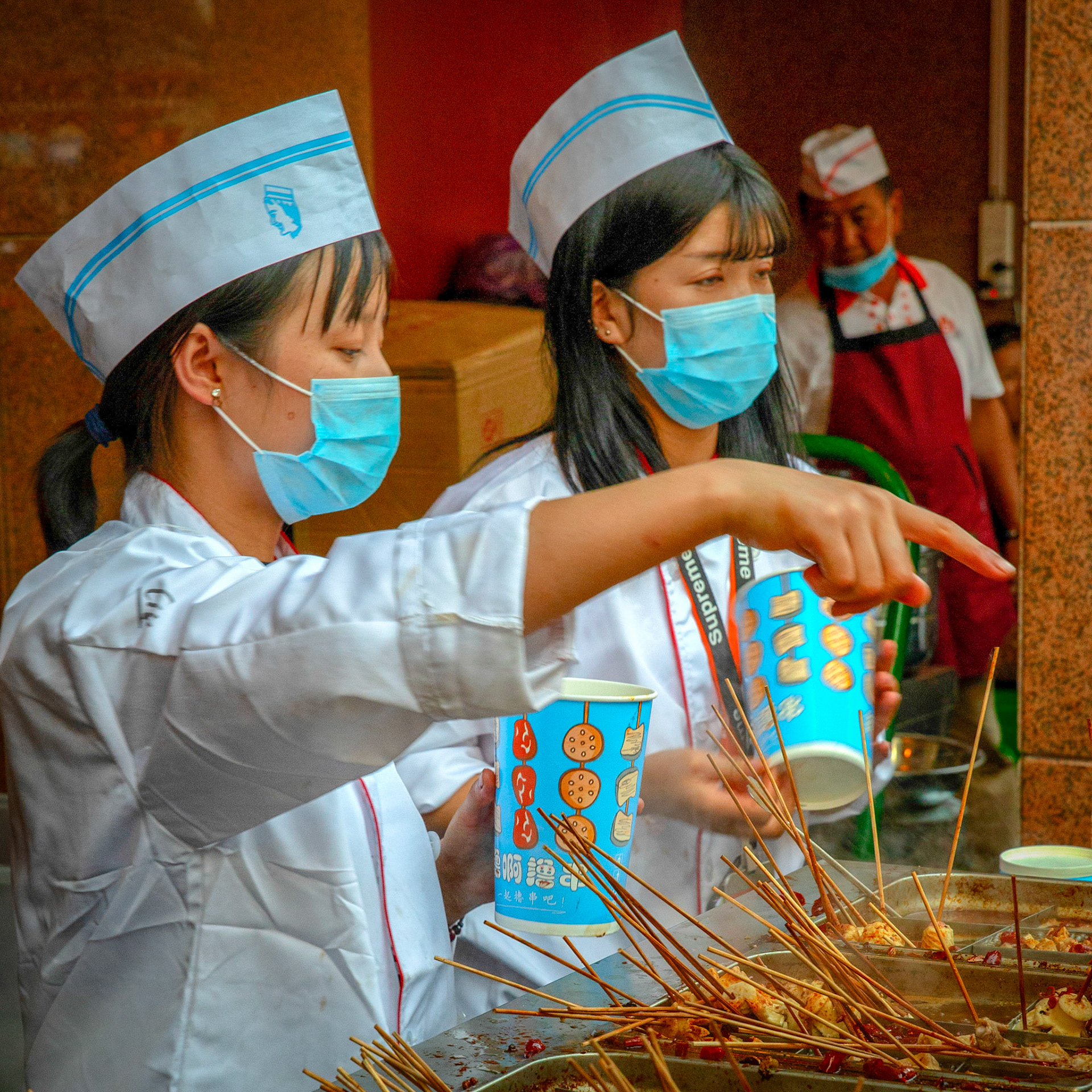 Urumqi, China - september 1, 2018 : Small shop selling snacks at the Urumqi grand bazaar. Girsl wearing face masks and hats.