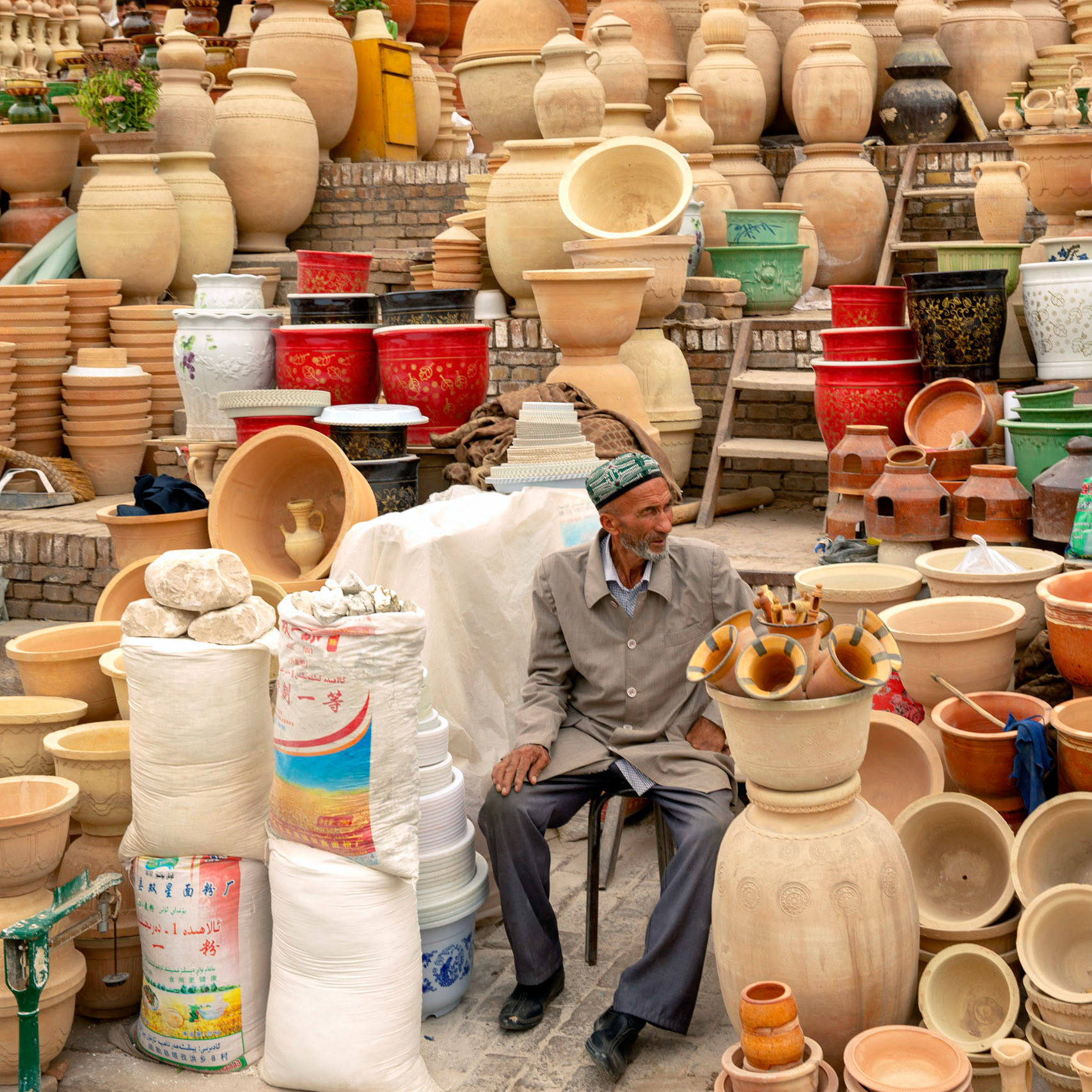 kashgar, Xinjiang, China - September 5, 2018: Man sitting in front of large pots and vases sold outdoors in Kashgar.