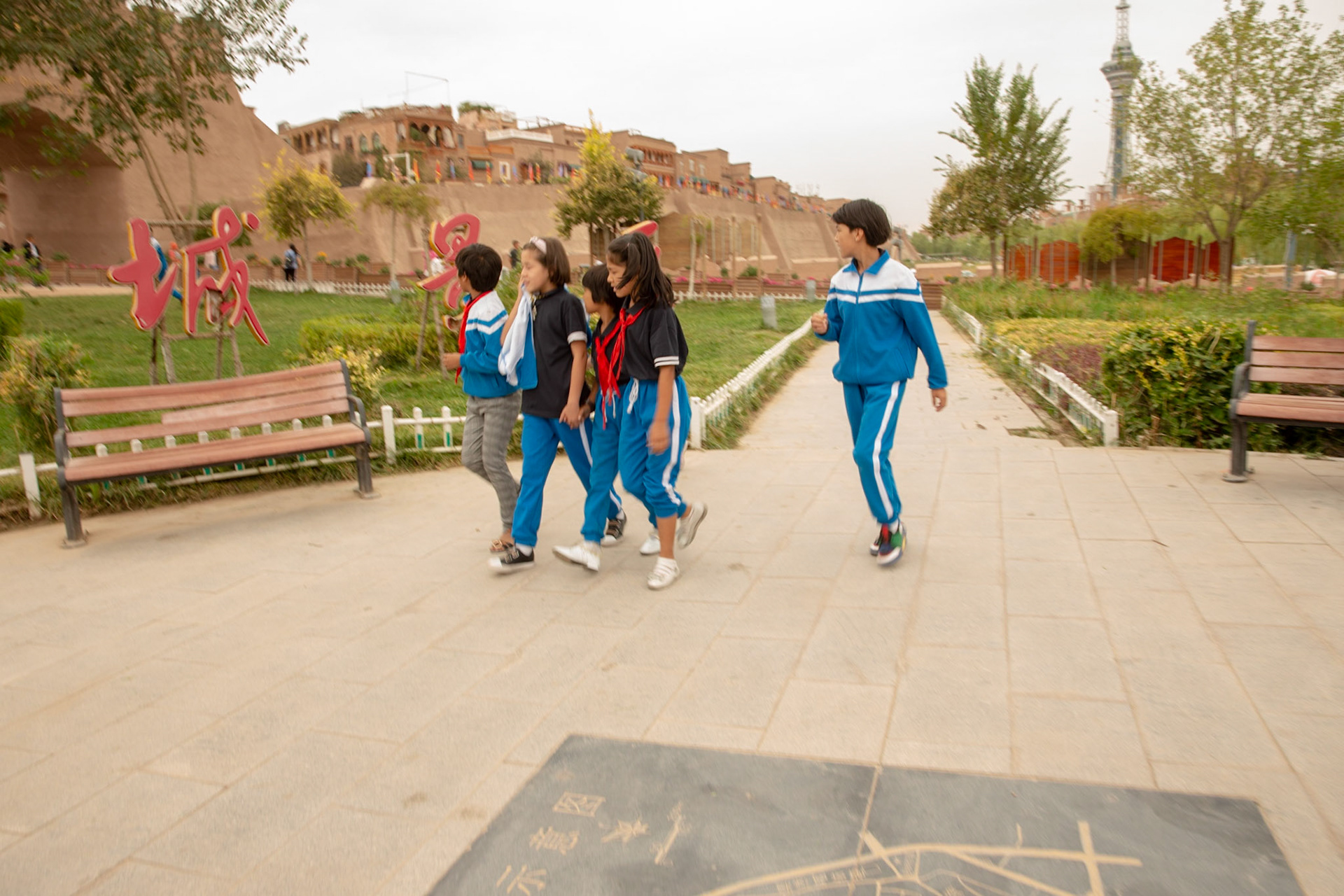 kashgar, Xinjiang, China - September 5, 2018: Children in school dress walking in front of large chinese characters in font of the big wall surrounding the rebuilt old city of Kashgar