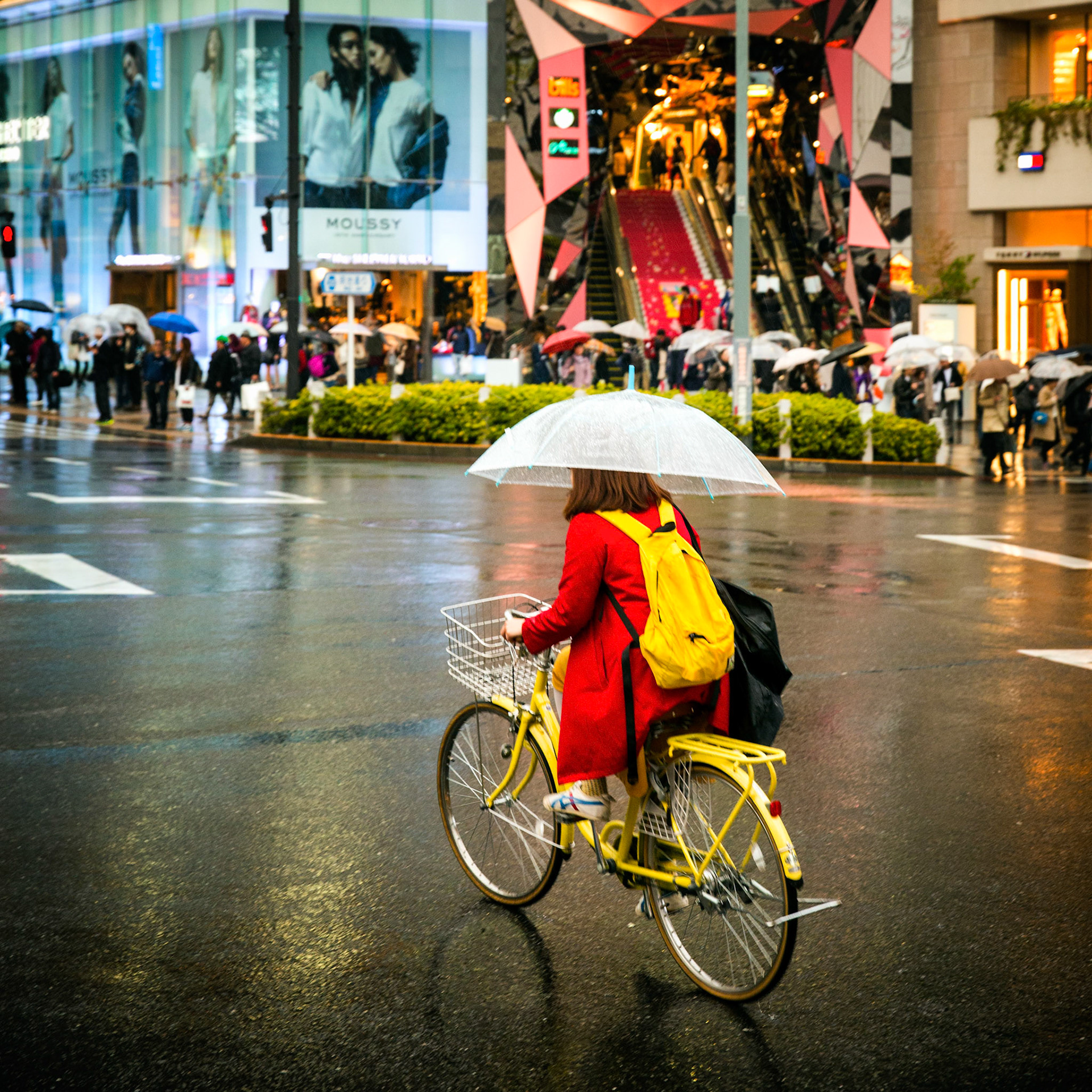 Tokyo, Japan - April 107, 2015 : Girl with yellow backpack riding a yellow bike, whilst holding an umbrella, in the Tokyo traffic. Crowd in the background