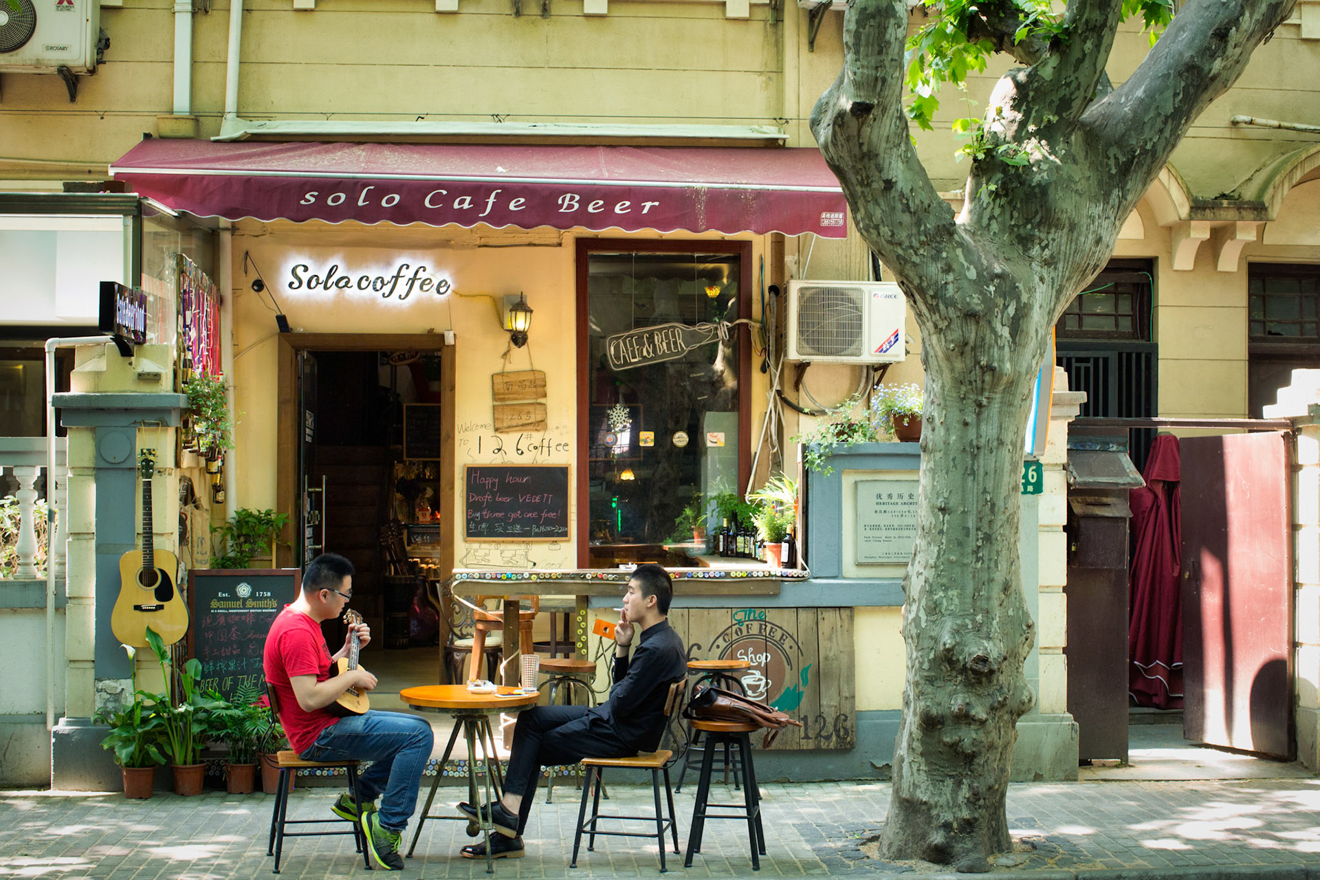 Shanghai, China - April 29th, 2016 : Two men sitting and relaxing at a Shanghai cofee bar, playing ukelele and smoking a cigarette