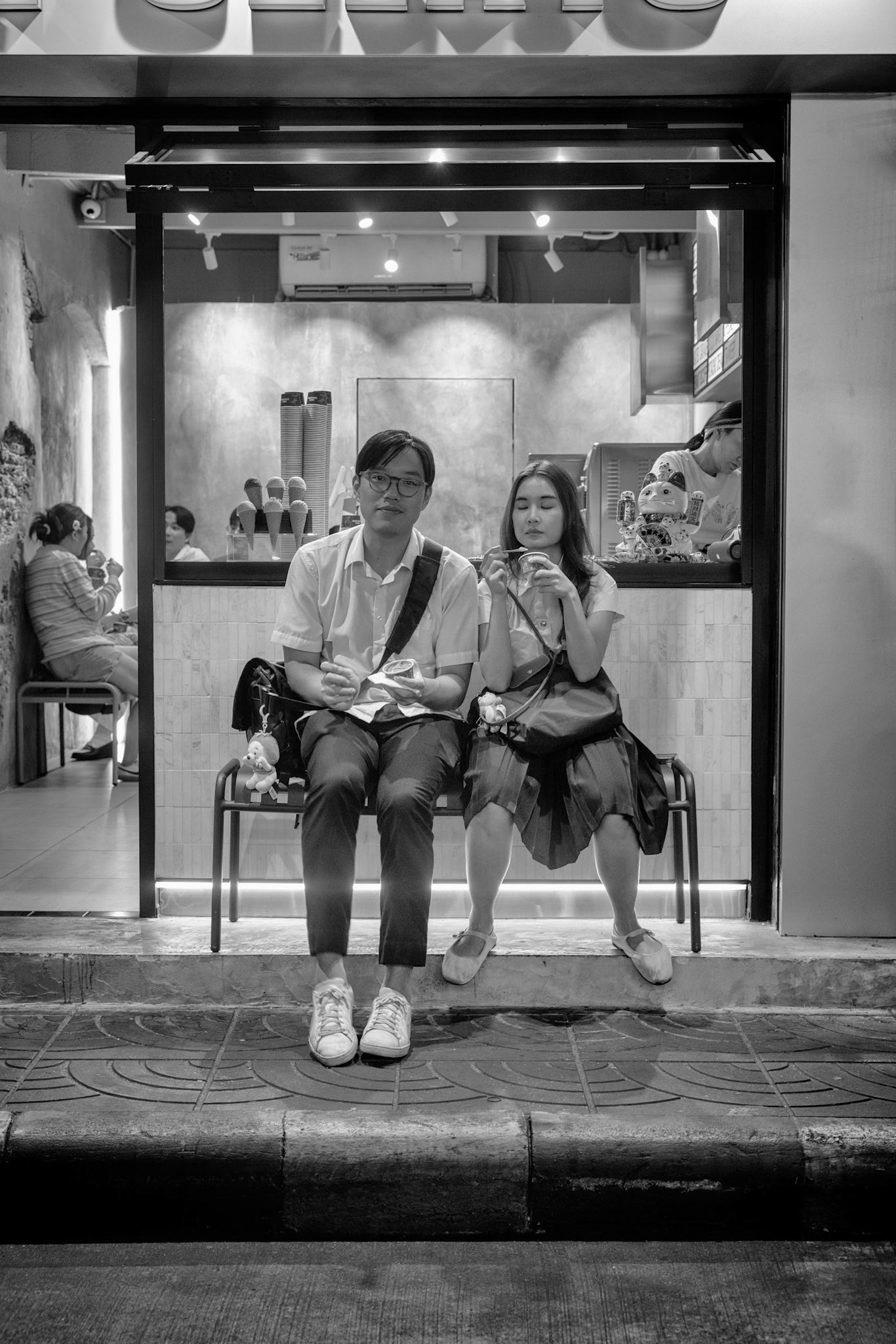 Bangkok, Thailand - January 14th 2025: A young couple enjoys ice cream while seated outside a dessert shop in Chinatown, taking a break from the lively street scene of the bustling neighborhood