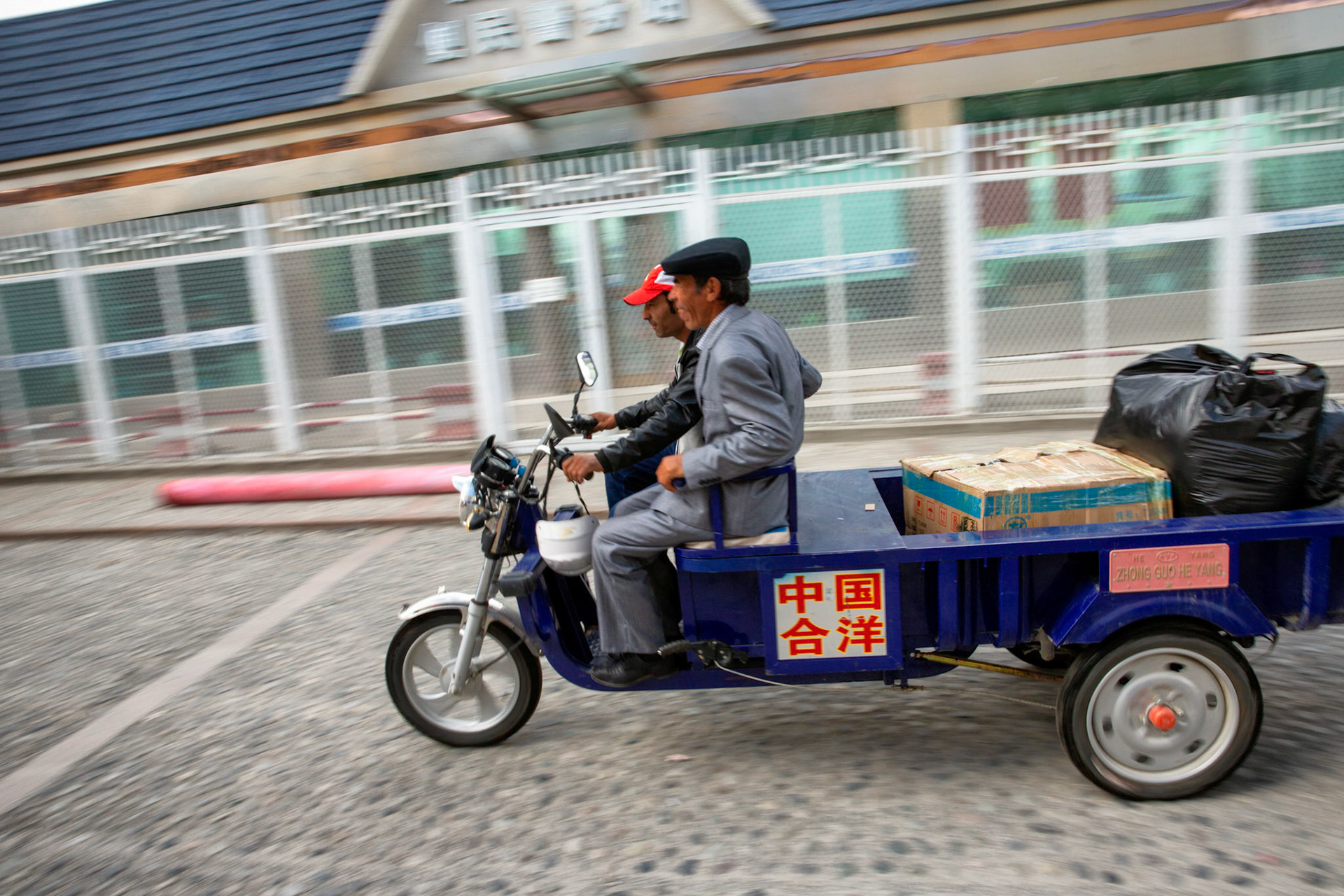 Tashgurkan, China - September 7th, 2018 : Two men sitting on a typical three-wheeled vehicle transporting goods