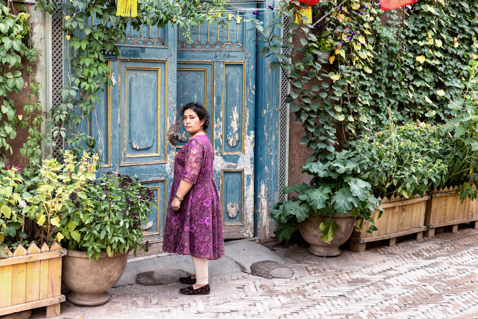 Kashgar,  China - September 10th, 2018 : Uyghur woman standing in front of a half open door in Kashgar's old city