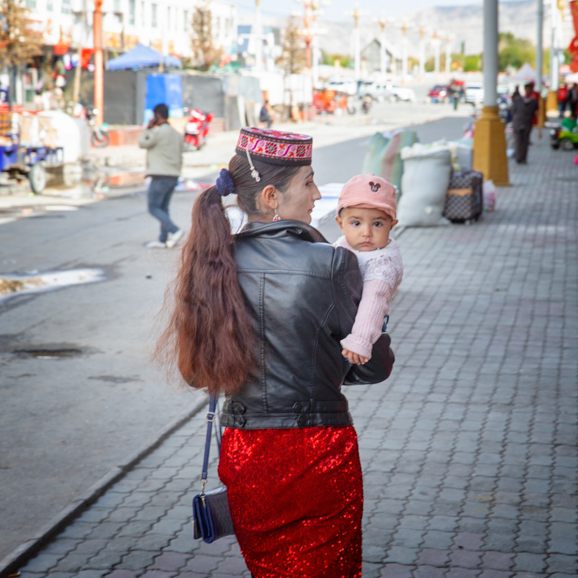 Tashgurkan, China - september 7th, 2018 : Woman wearing a hat typical for that region, carrying a young child in the main street of Tashkurgan.