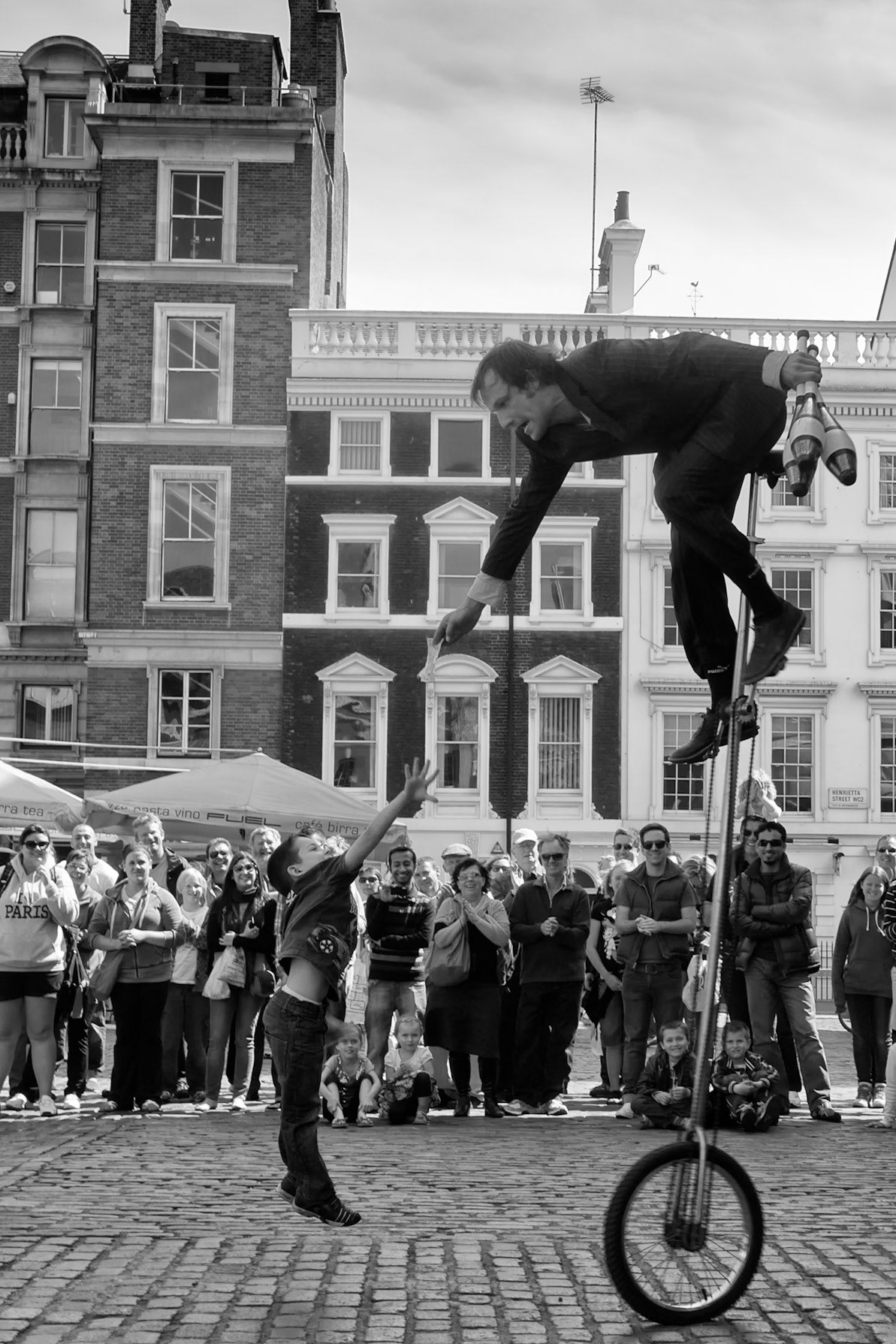 London, United kingdom - May 1, 2011 :  Unicyclist and performer Richard Garaghty performing his show in Covent Garden. giving a 5 pound note to a boy who has assisted him in his show. The boy jumping up to reach the banknote. Richard  (35) has been performing as a street performer for 17 years, as well as performing in venues such as the Edinburgh fringe festival, the Cape Town street festival and in the rolling Stones World Rock tour.