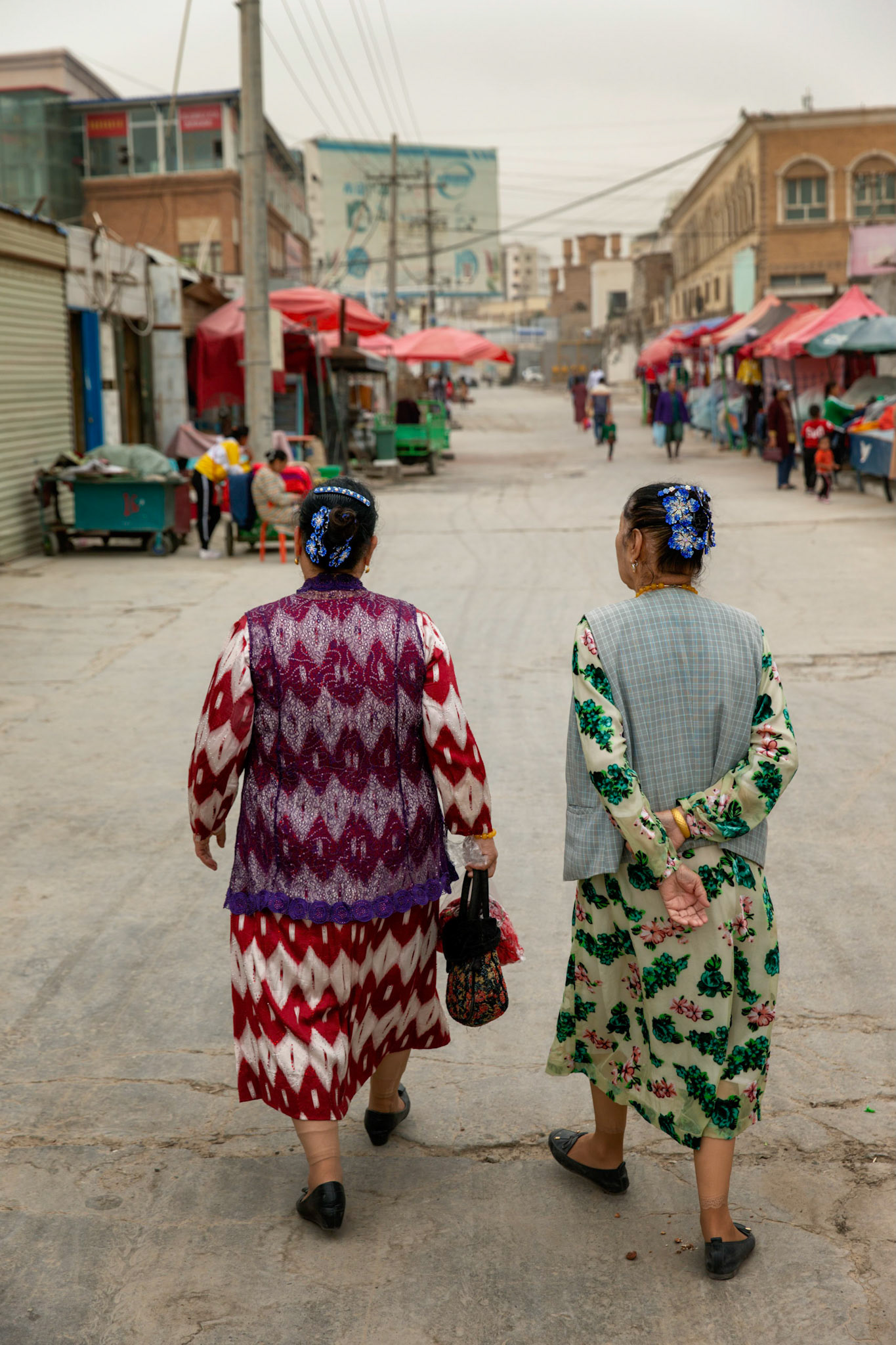 Hotan, China - September 13th 2018 :  Uyghur women seen from behind, walking on a street in Hotan, shops in the background