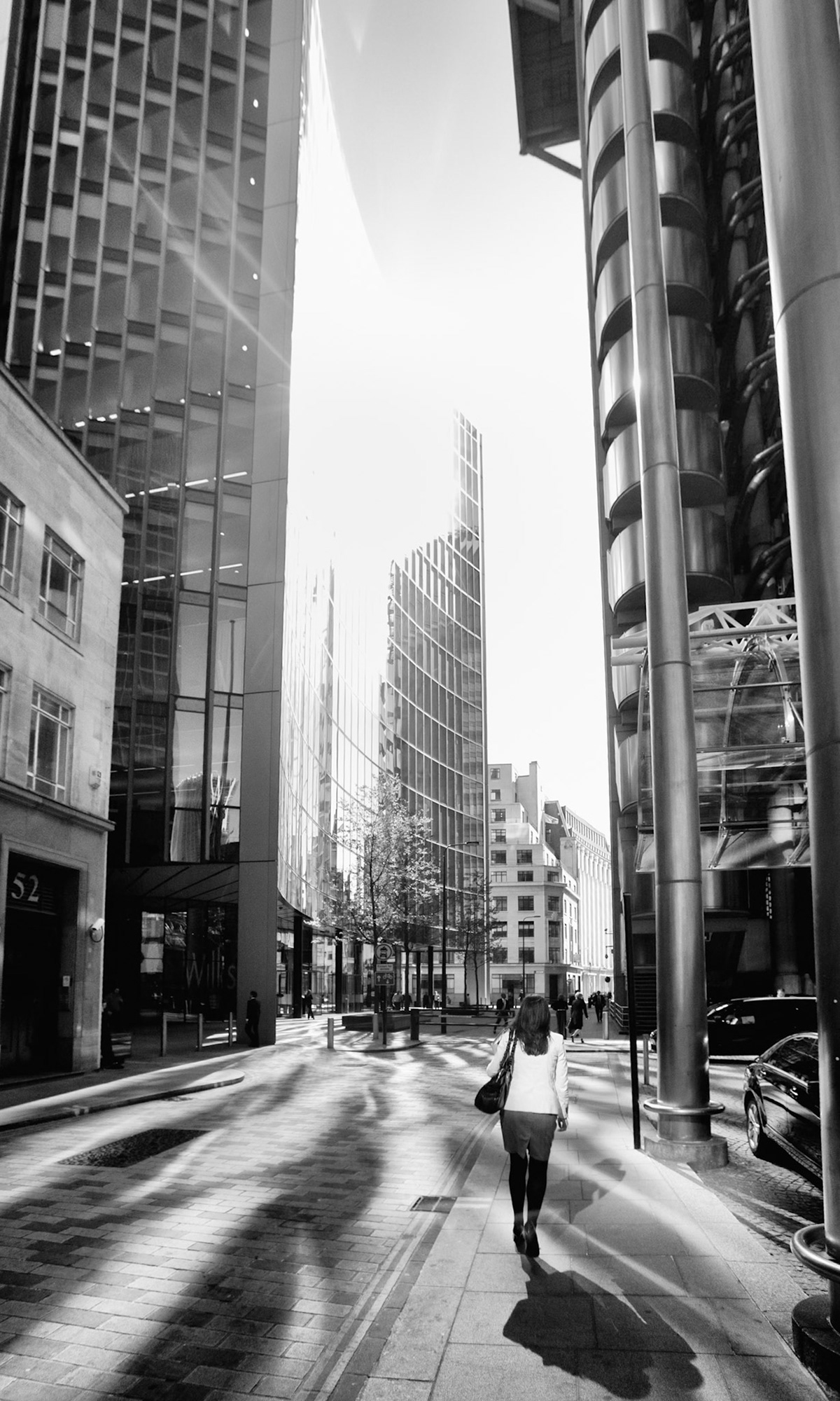 London, United Kingdom - May 3, 2011  - Young woman walking in front of the Lloyds building, London. Low sunlight reflected on buildings in the area casting a multitude of shadows. The Lloyds building is home to an insurance institure and is an example of modern architecture. Colour image converted to black and white, to remove the impact of colour lens flare.