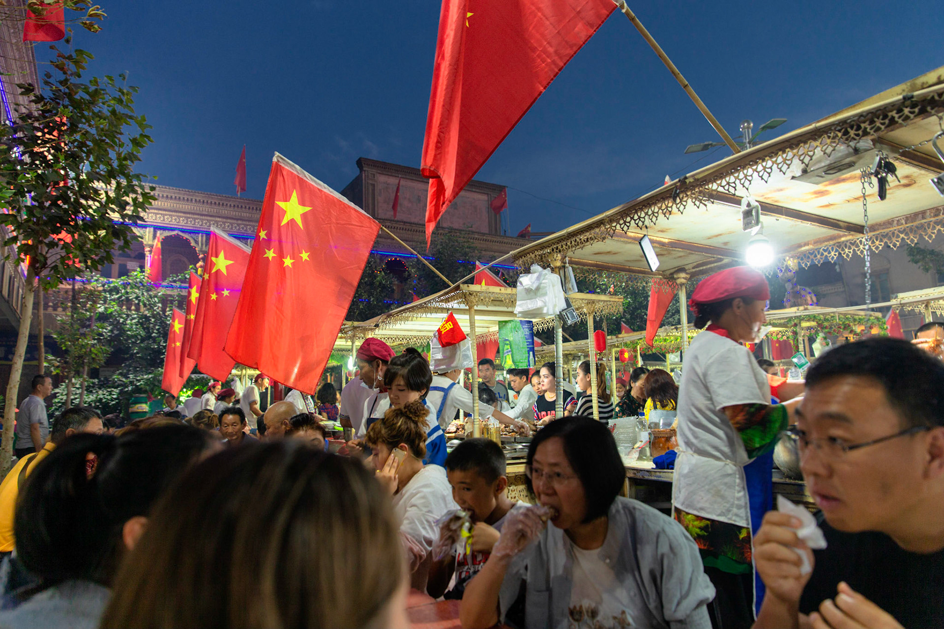 Kashgar,  China - September 10th, 2018 : Tourists and visitors eating food at the Kashgar evening food markeet, note the abundance of chinese flags