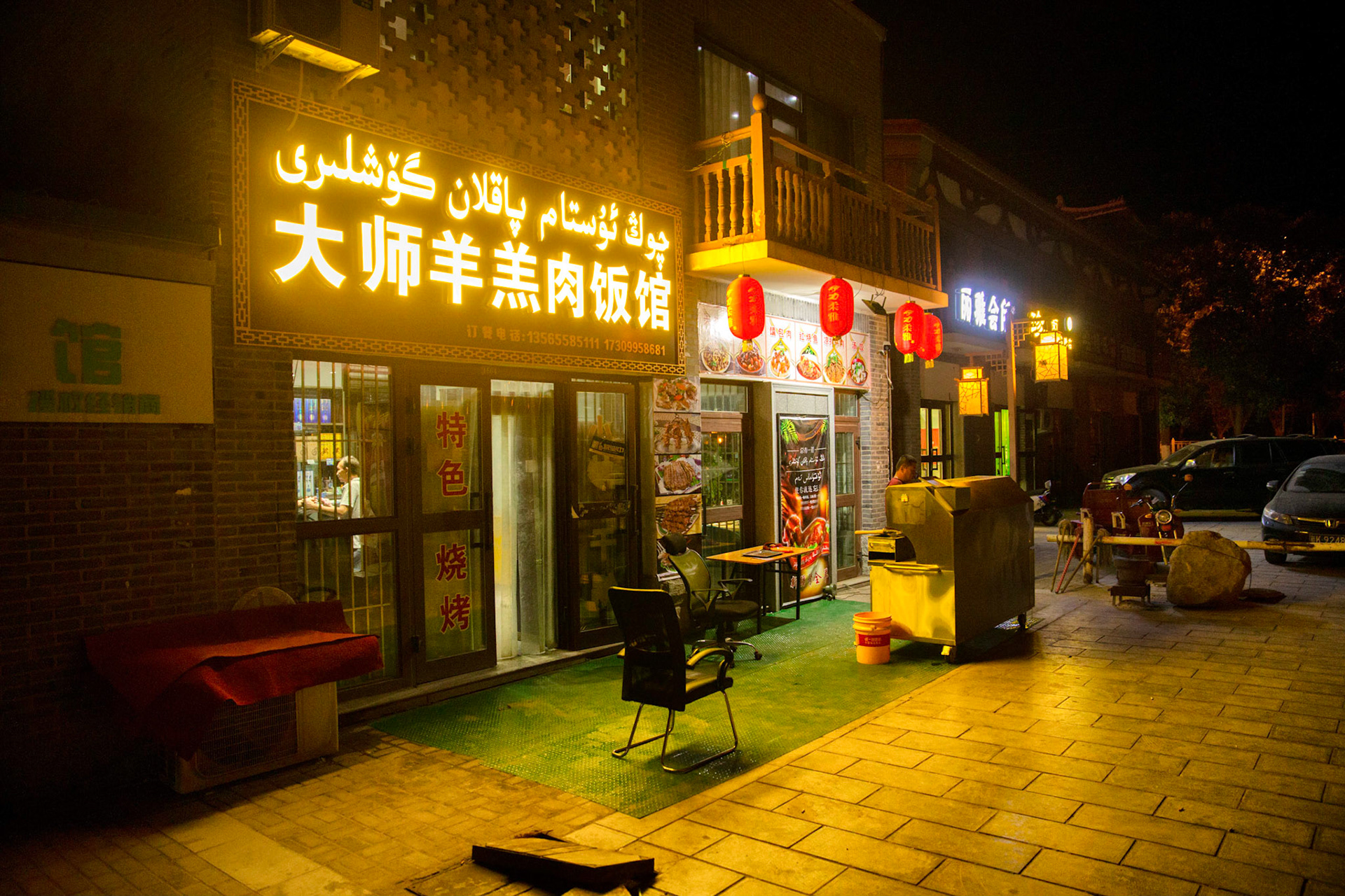 Shanshan, Xinjiang, China - september 2, 2018: Small restaurants at night in Shanshan (grainy image), cars parked in the background, note the signage is both in chinese and arab.