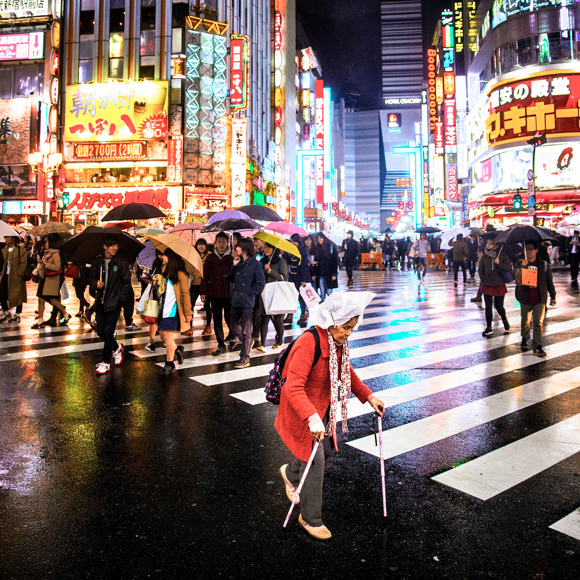 Tokyo, Japan - April 10, 2015 : Old woman with a plastic bag on her haid against the rain, two walking sticks, at  tokyo zebra crossing, crowd and neon light in the background