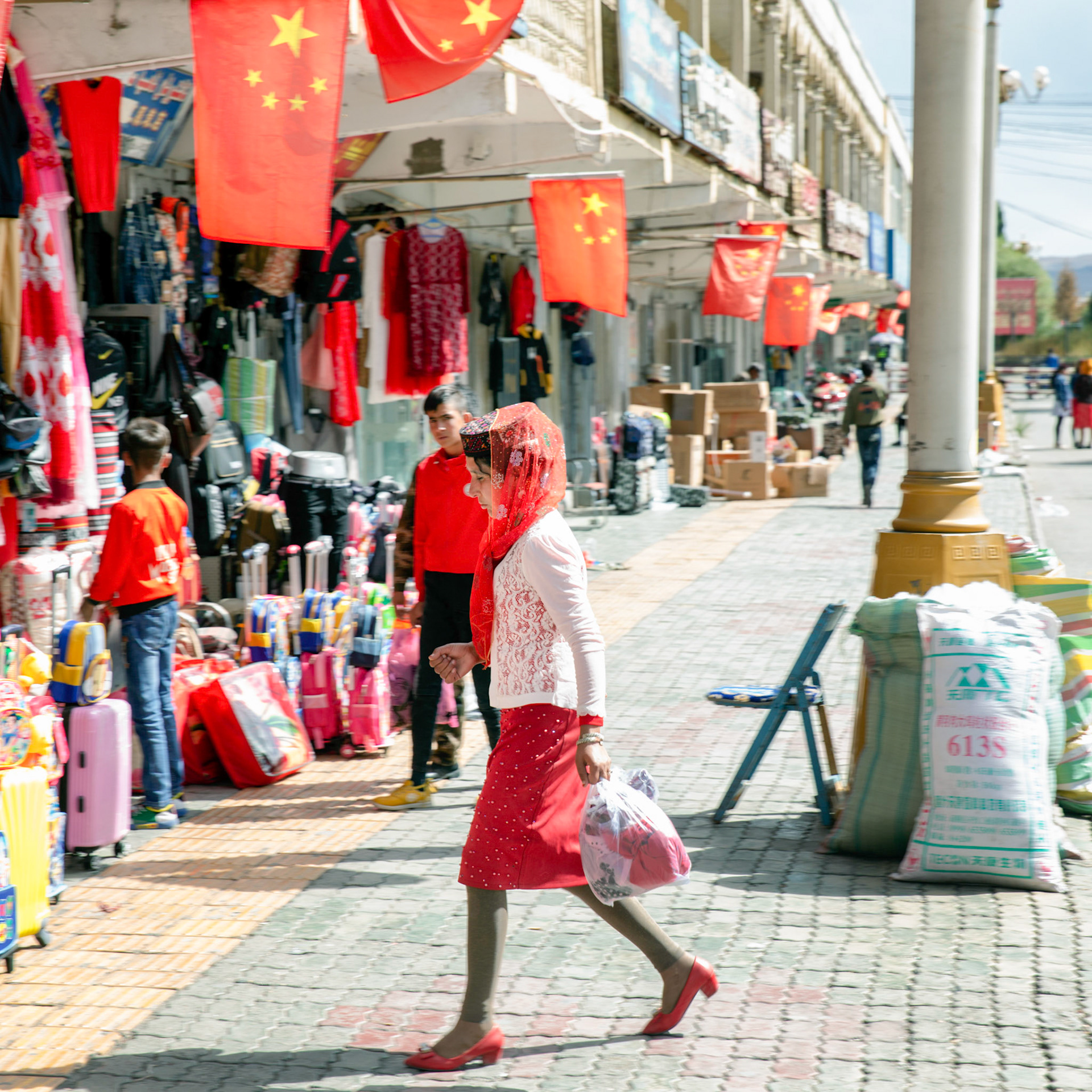 Tashgurkan, China - September 7th, 2018 : Woman wearing typical dress for the area, crossing the road in Tashgurkan.