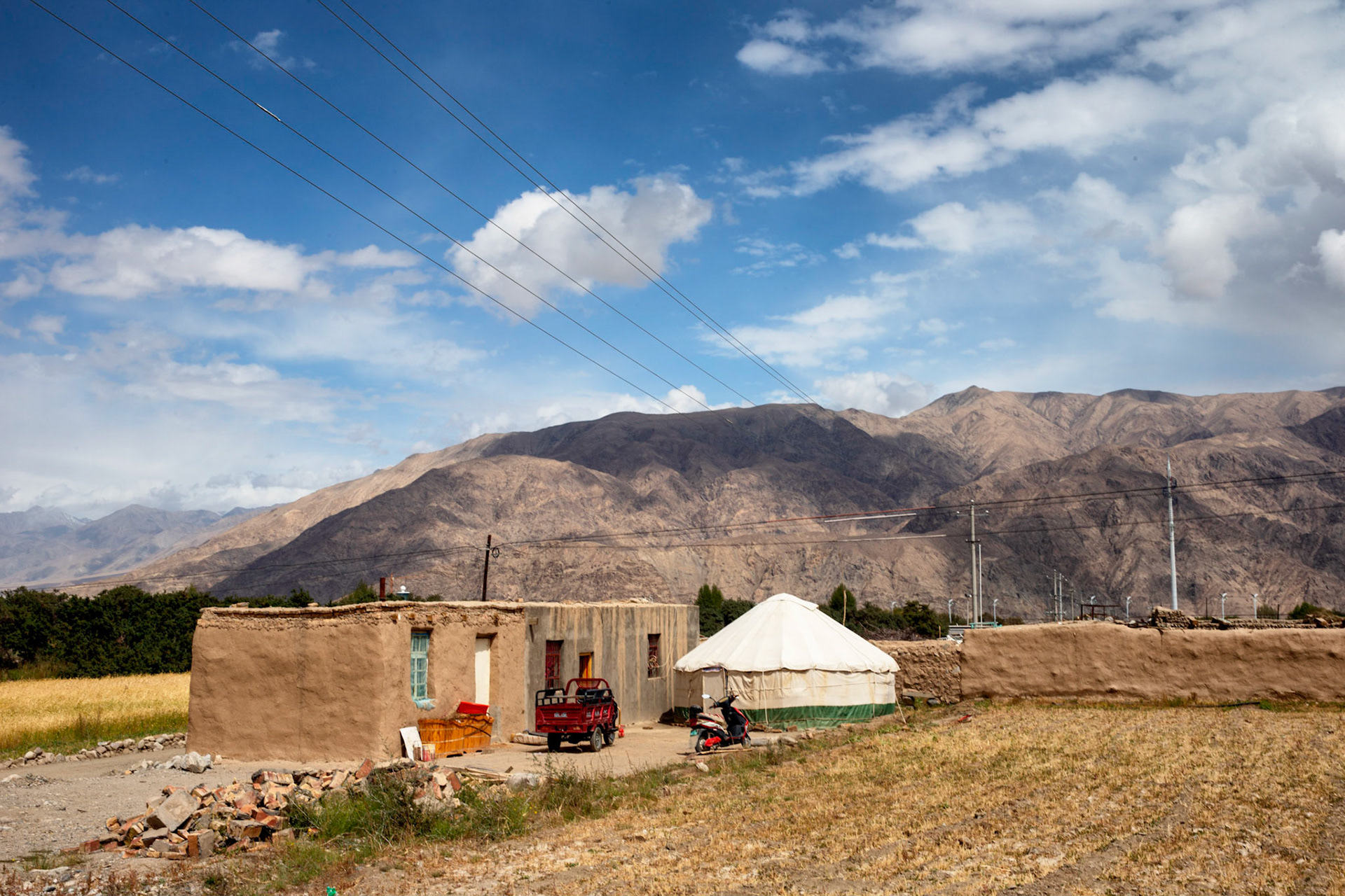 Tashgurkan, China - September 7th, 2018 : Typical small famhouse with Yurt. The yurt in this case is being used as a tool shed. Scooter and threewheeler parked behind the house.