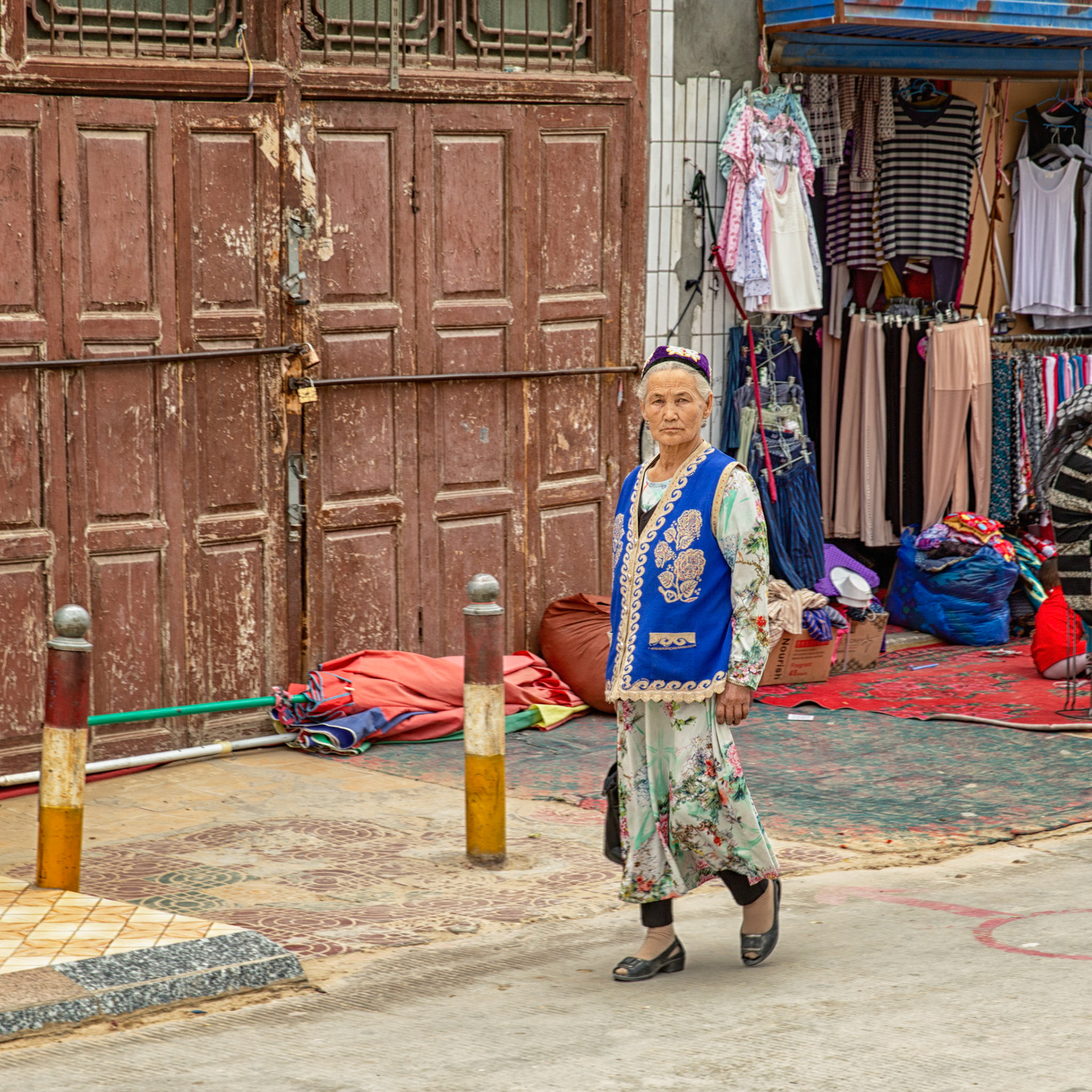 Hotan, China - September 13th 2018 :  Uyghur woman walking in taditional clothes in font of a textile shop