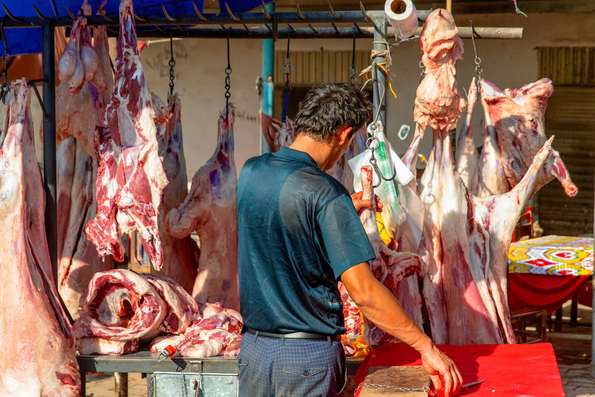 Kashgar,  China - September 9th, 2018 : Butcher preparing to carve meat in the Kashgar market, note the knive is chained to the table.