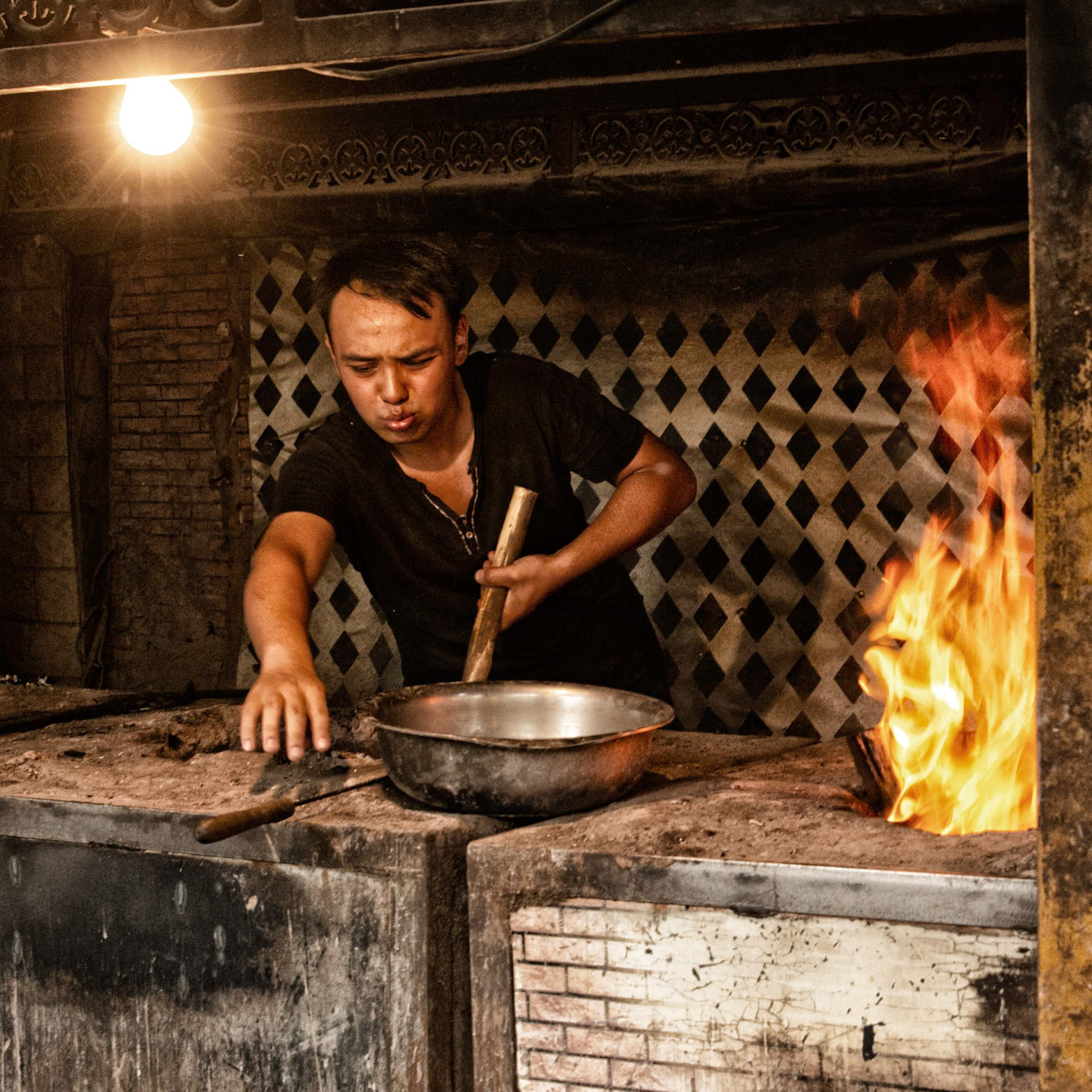 Kashgar, Xinjiang, China - September 5, 2018: Man cooking food on a fire stove in one of the many steet food places in Kashgar.