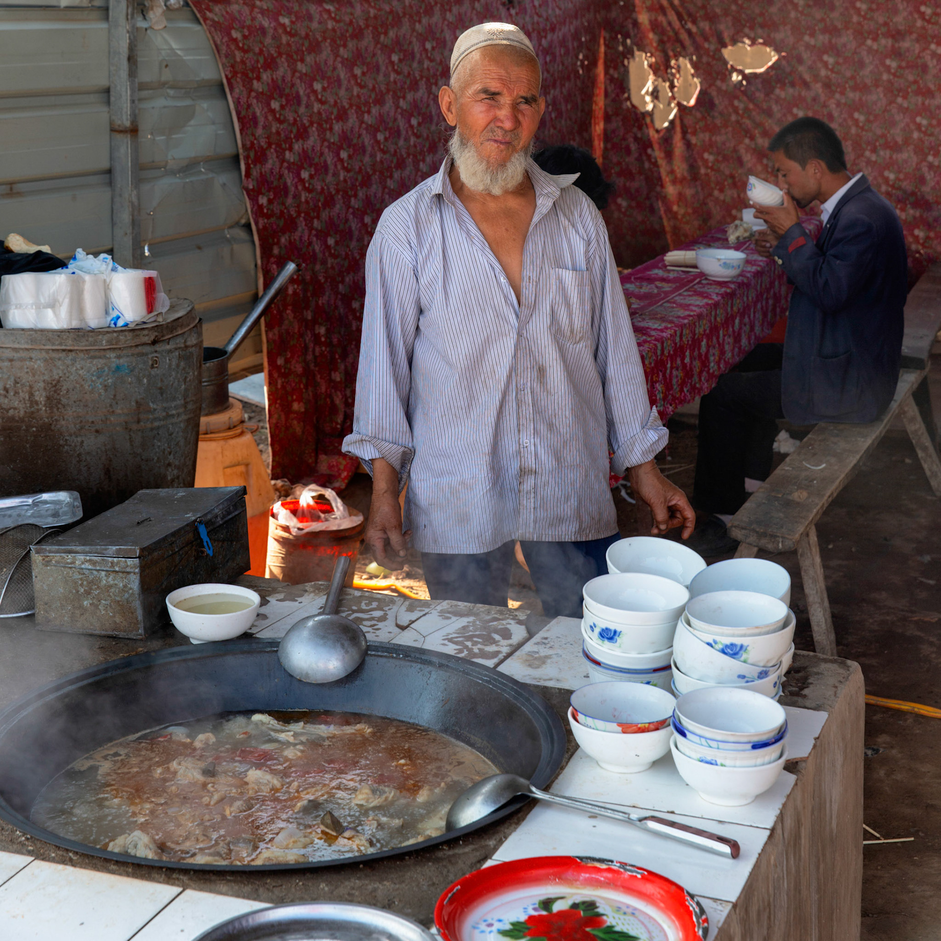 Kashgar,  China - September 9th, 2018 : Cooking lamb soup in  Kashgar, client drinking soup in the background.