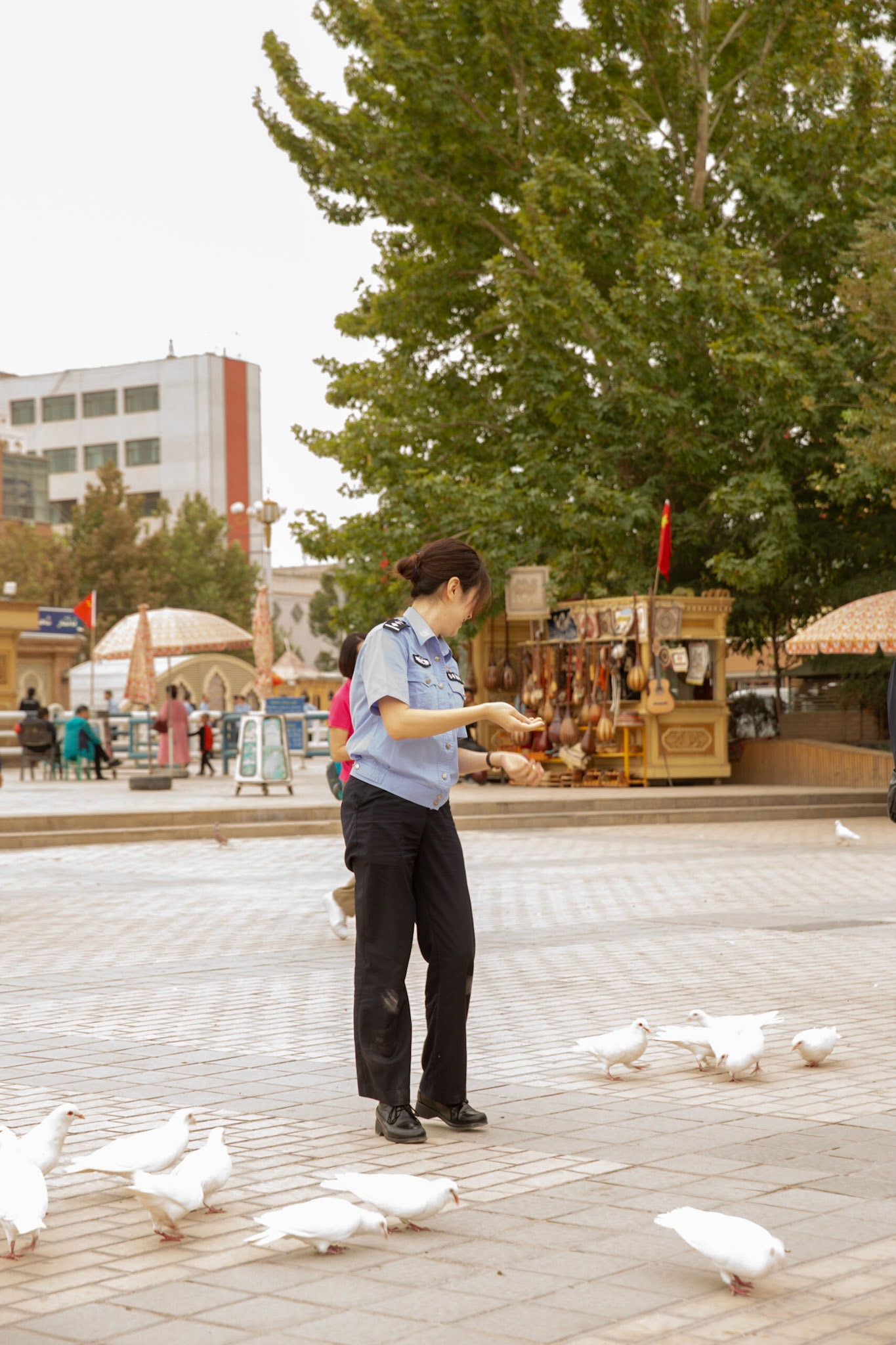 kashgar, Xinjiang, China - September 5, 2018: chinese police woman feeding doves in front of some tourist shops in Kashgar