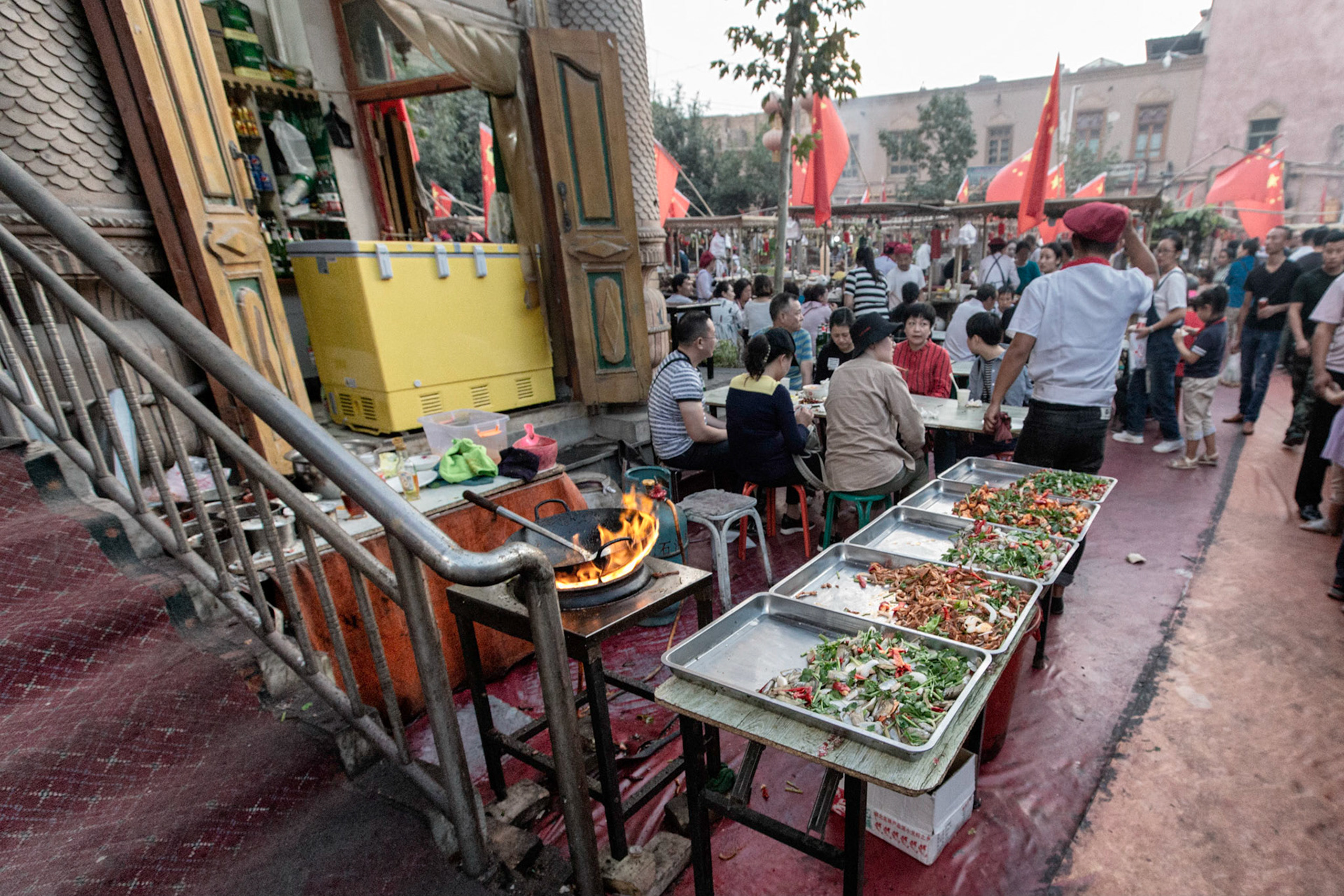 Kashgar,  China - September 11th, 2018 : People sitting and eating food at the Kashgar food market, note the many chinese flags