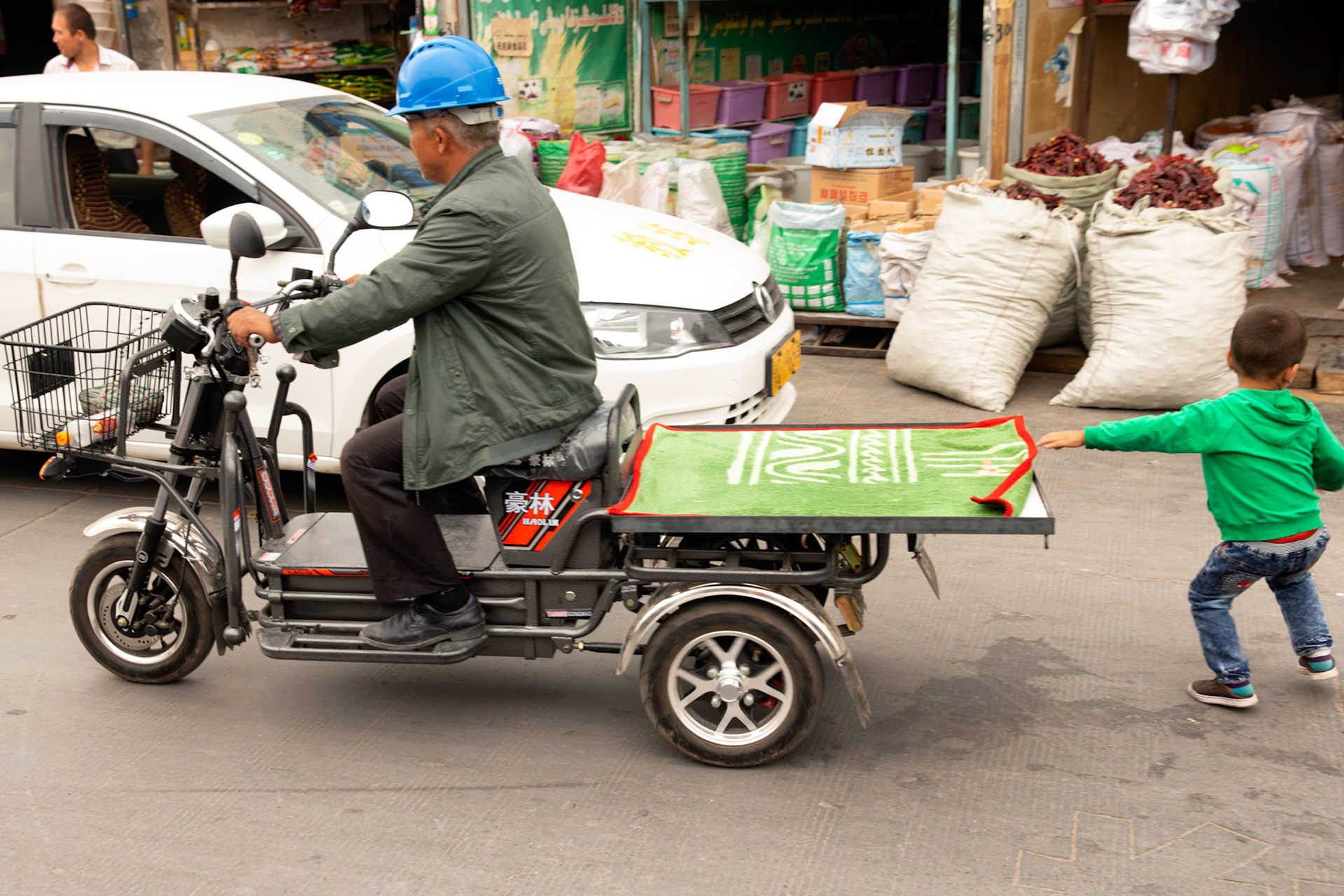 Kashgar, Xinjiang, China - September 5, 2018: Little boy grabbing a 3 wheeler with a man wearing a safety helmet