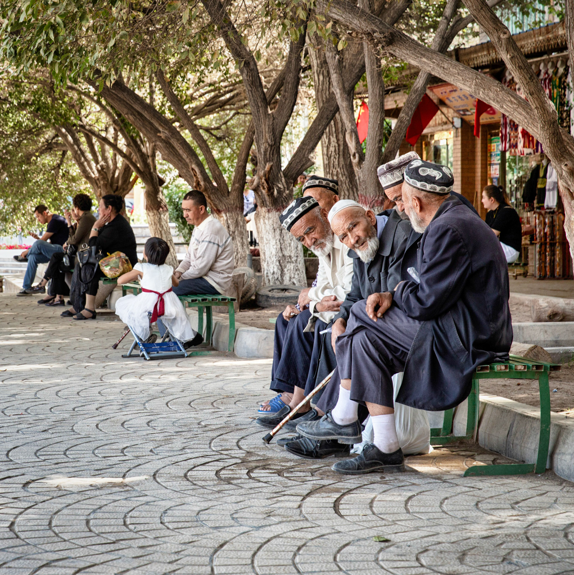 Kashgar,  China - September 9th, 2018 : Uyghur men chatting on a bench in one of the tree lined streets in Kashgar's renewed old city