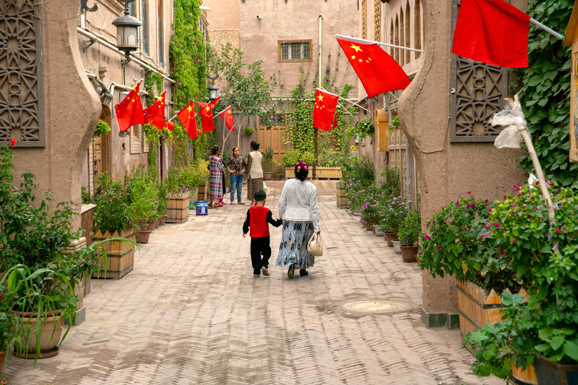 Kashgar, Xinjiang, China - September 5, 2018: Woman walking in one of the rebuilt streets in Kashgar Old City. CHinese flag on te wall and inscriptions in both chinese as well as arab/uyghur language.
