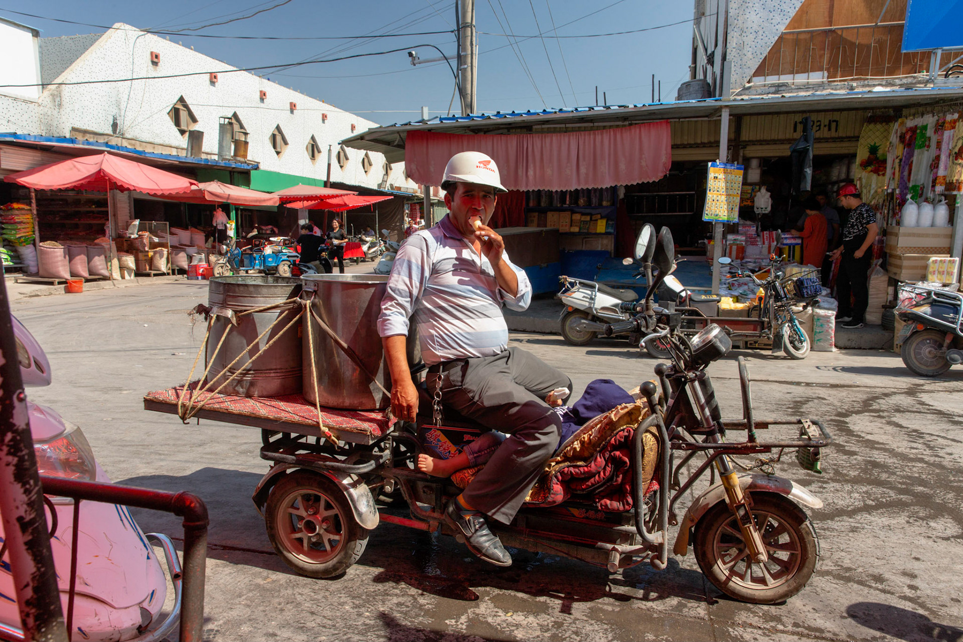 Kashgar,  China - September 10th, 2018 : Man wearing a hard hat enjoying an ice cream sitting on his three wheel motorcycle in the Kahgar grand bazaar.