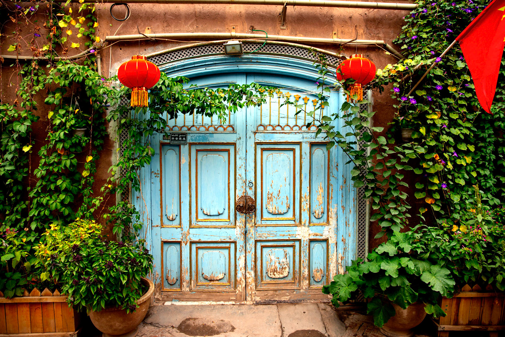 Kashgar, Xinjiang, China - September 5, 2018: Door, bearing a small sign saying "peaceful family"in one of the rebuilt streets in Kashgar Old City. CHinese flag on te wall and inscriptions in both chinese as well as arab/uyghur language.