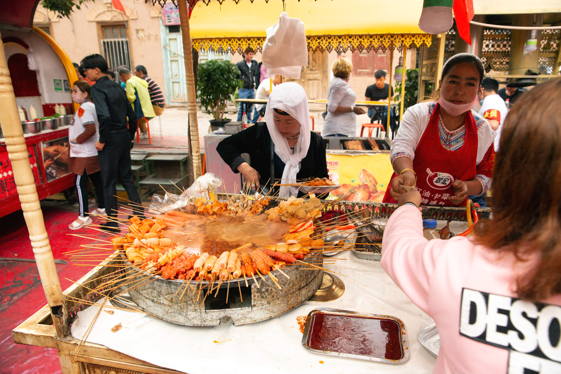 kashgar, Xinjiang, China - September 5, 2018: Food stall Kasghar food market, grill sticks with vegetables and meat, people preparing food and serving food, tourists in the background