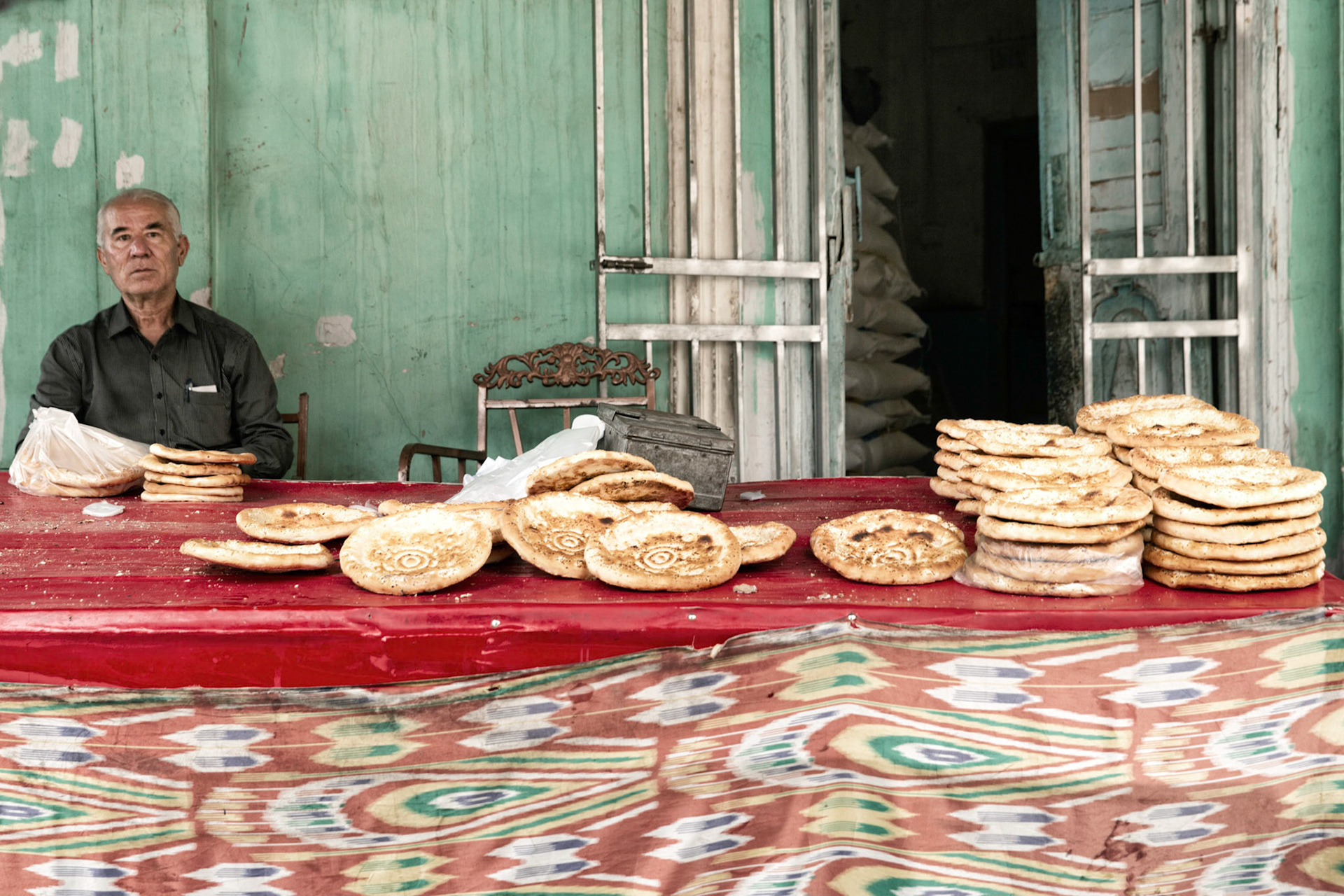Kashgar, Xinjiang, China - September 5, 2018: Uyghur man selling nan bread in a street in Kashgar, stacks of the typical bread laid out on a large table.