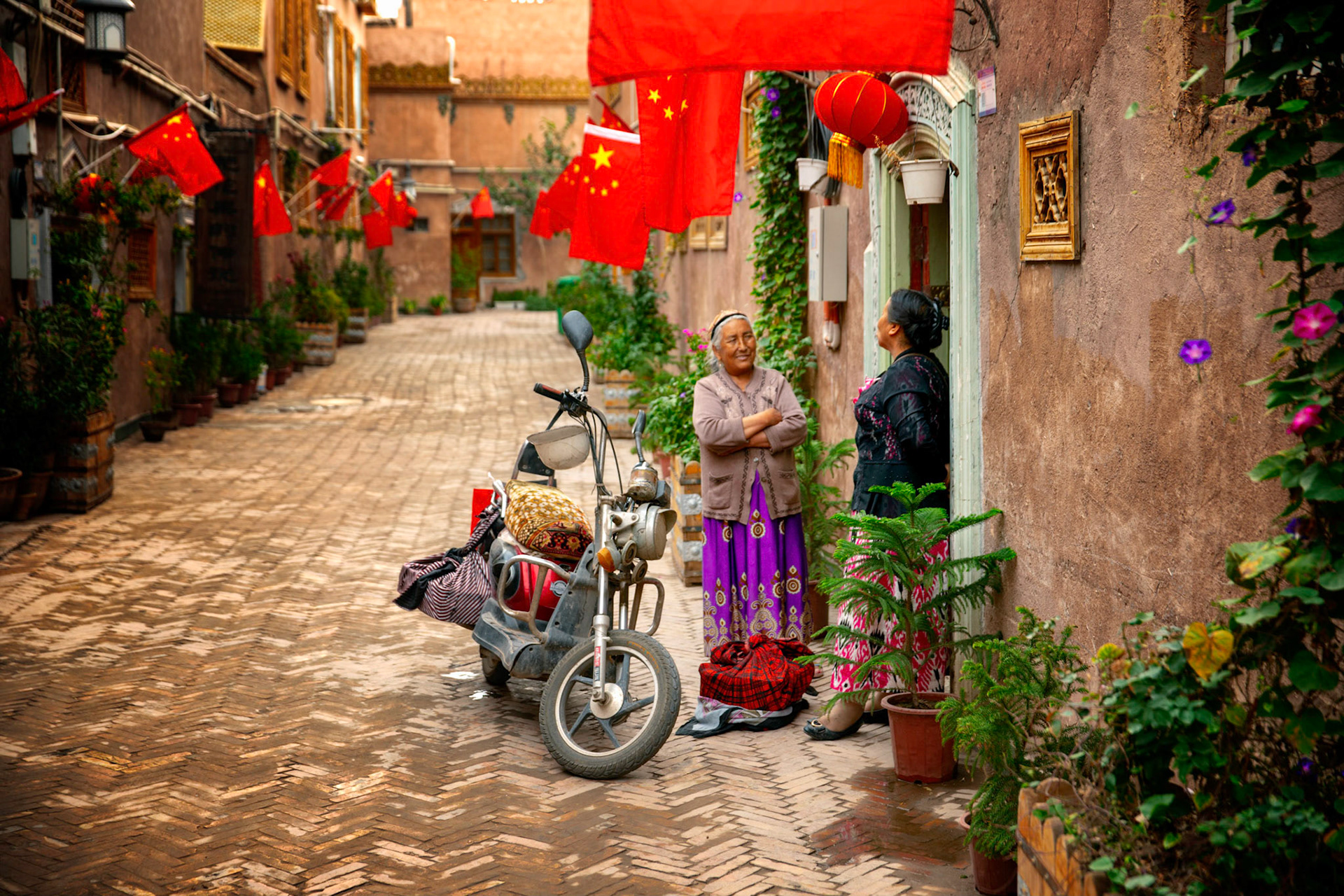 Kashgar, Xinjiang, China - September 5, 2018: Two women chatting in an open doorway, in one of the chinese flag littered streets in the newly reconstructed old town of Kashgar.