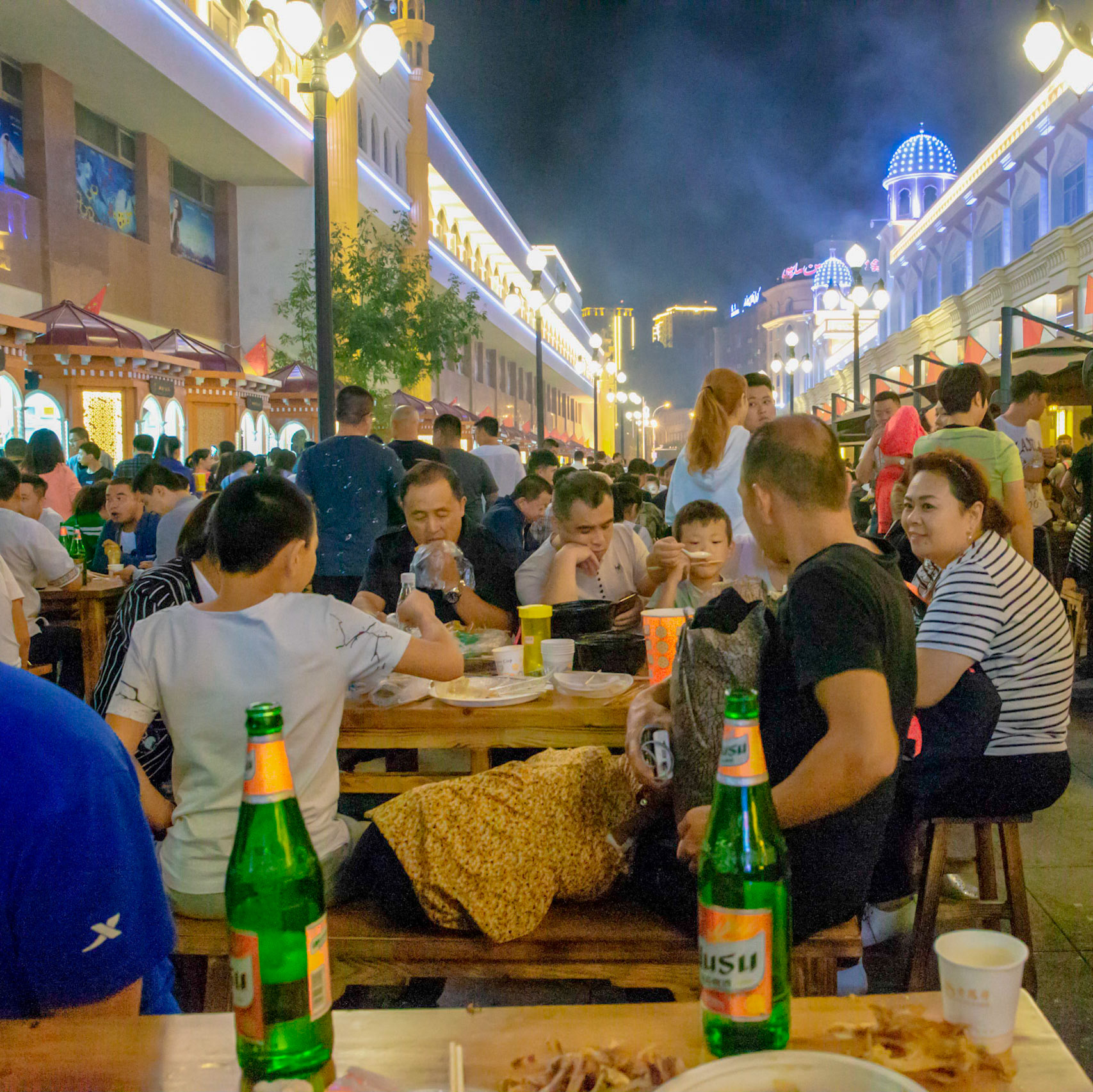 Urumqi, China - september 1, 2018 : People eating food an drinking beer just outside the grand bazaar in Urumqi, the street food stalls are very busy and people gather food from various stalls and eat it together at one of the tables.