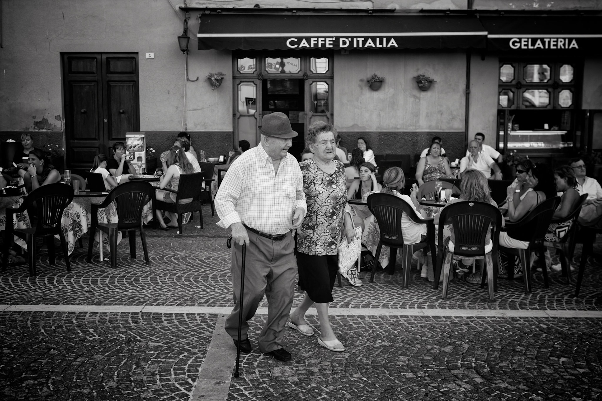 Cagli, Italy - July 29th 2012: senior couple walking across the cobblestones of Cagli village square in front of the local ice cream cafe. Tourists and locals in the background  [url=http://www.istockphoto.com/search/lightbox/11293042#64eec1d][img]http://www.piebinga.nl/banners/italy.jpg[/img][/url]